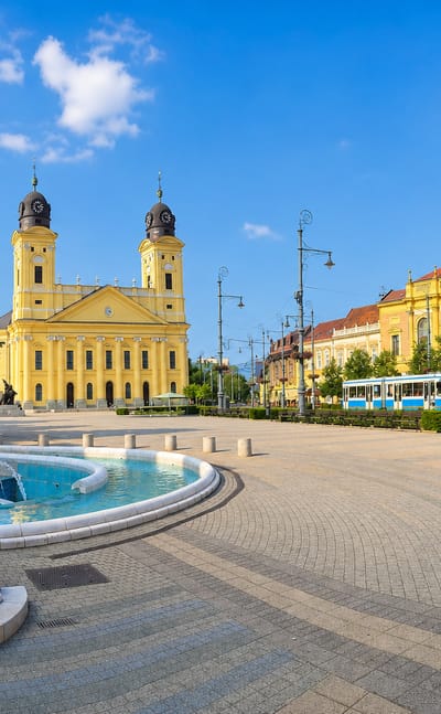Debrecen's yellow twin-towered Great Reformed Church and fountain on Kossuth Square with a passing tram.