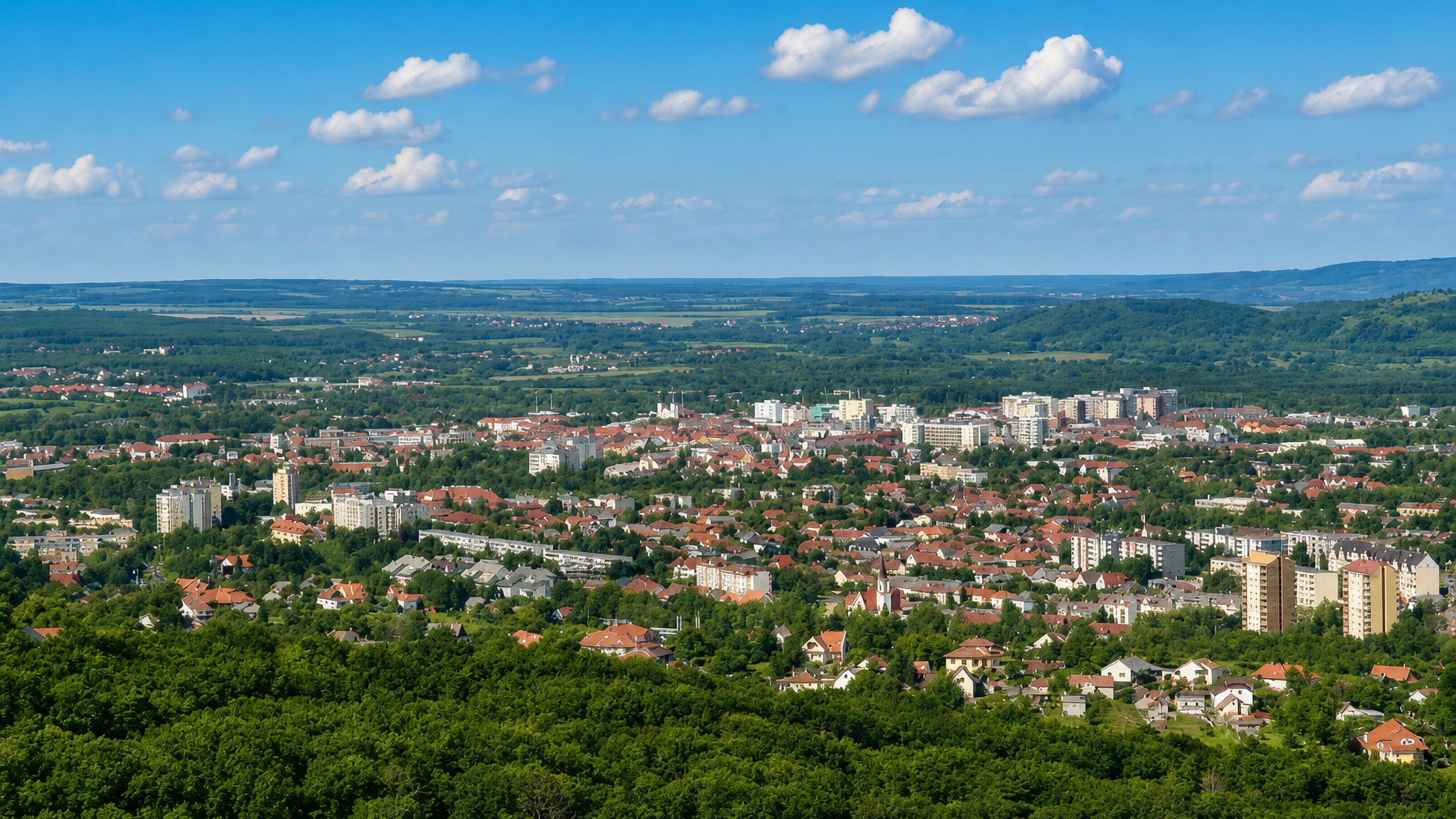 Zalaegerszeg's red roofs, church spires and housing blocks below wooded Zala hills in western Hungary.