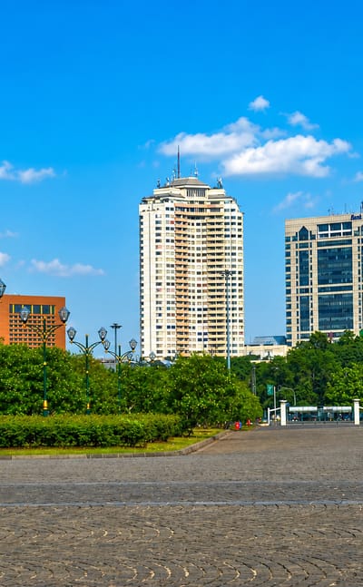 A broad paved plaza fringed by trees fronts office towers in Central Jakarta under a bright blue sky.