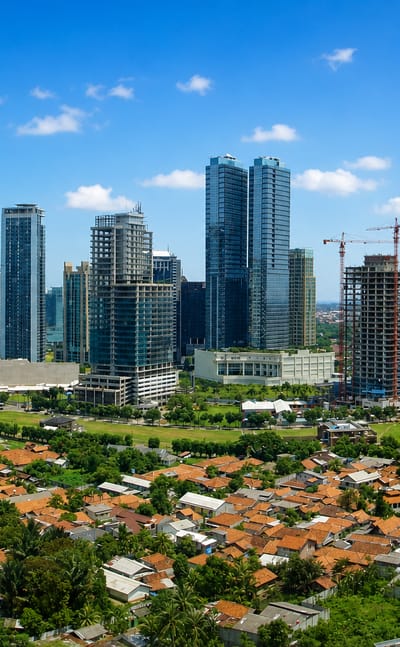 Mega Kuningan business-district towers rising above low red-roofed neighbourhoods in Jakarta under a blue sky