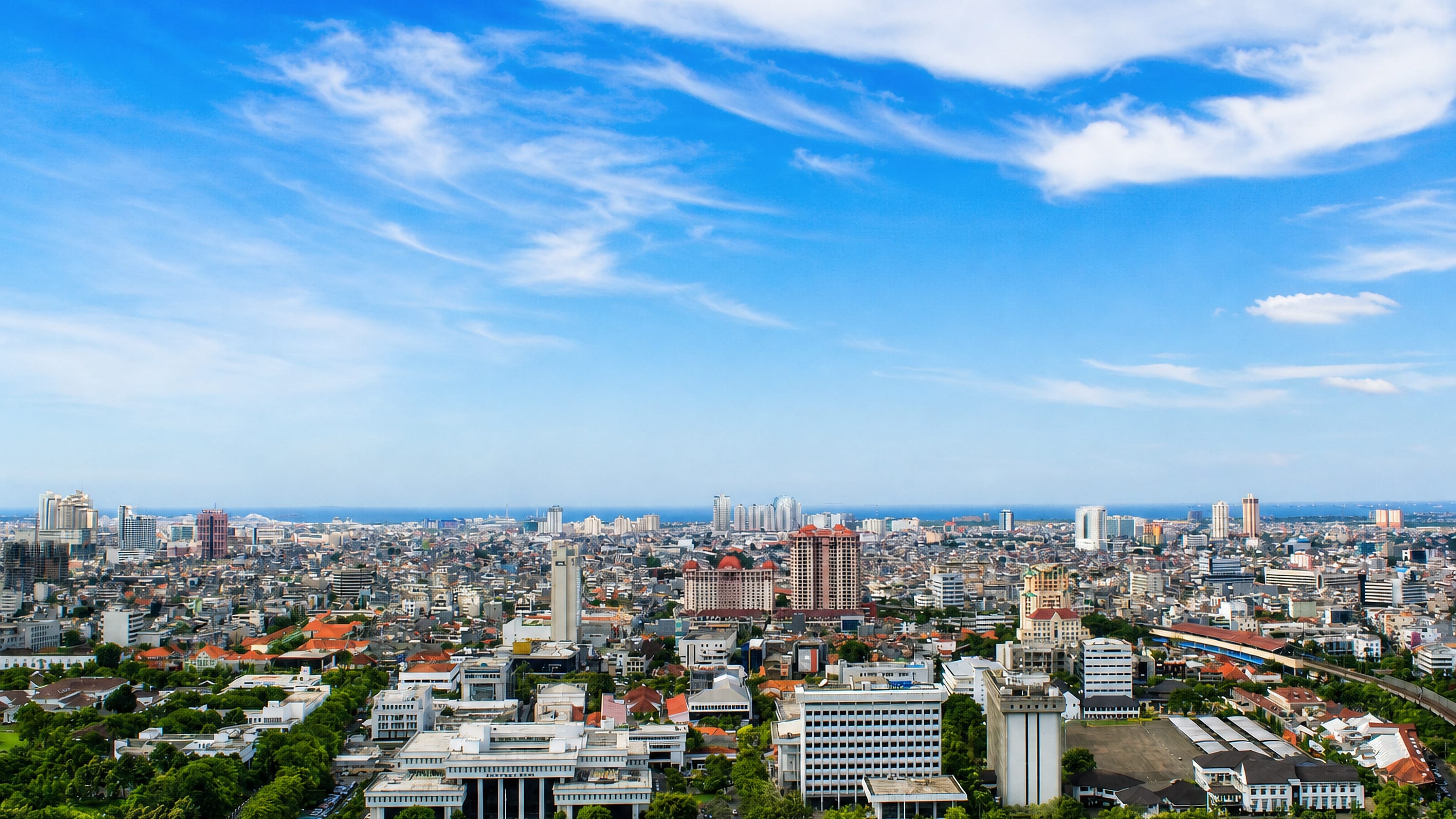 Wide daytime view over dense low-rise rooftops and scattered towers toward the sea in North Jakarta, Indonesia