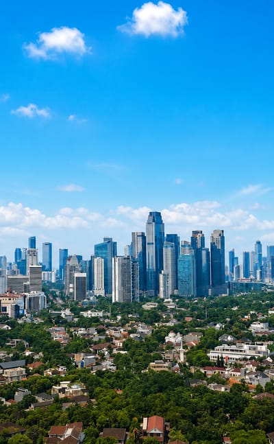 Glass high-rise towers of South Jakarta's business districts rise behind leafy low-rise residential neighborhoods by day.