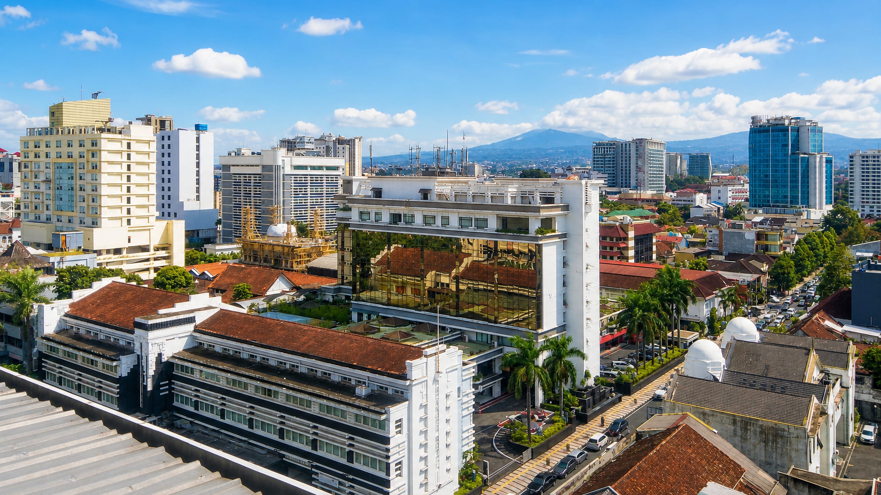 Bandung rooftops and art deco facades under a blue sky, with volcanic mountains rising behind the city centre