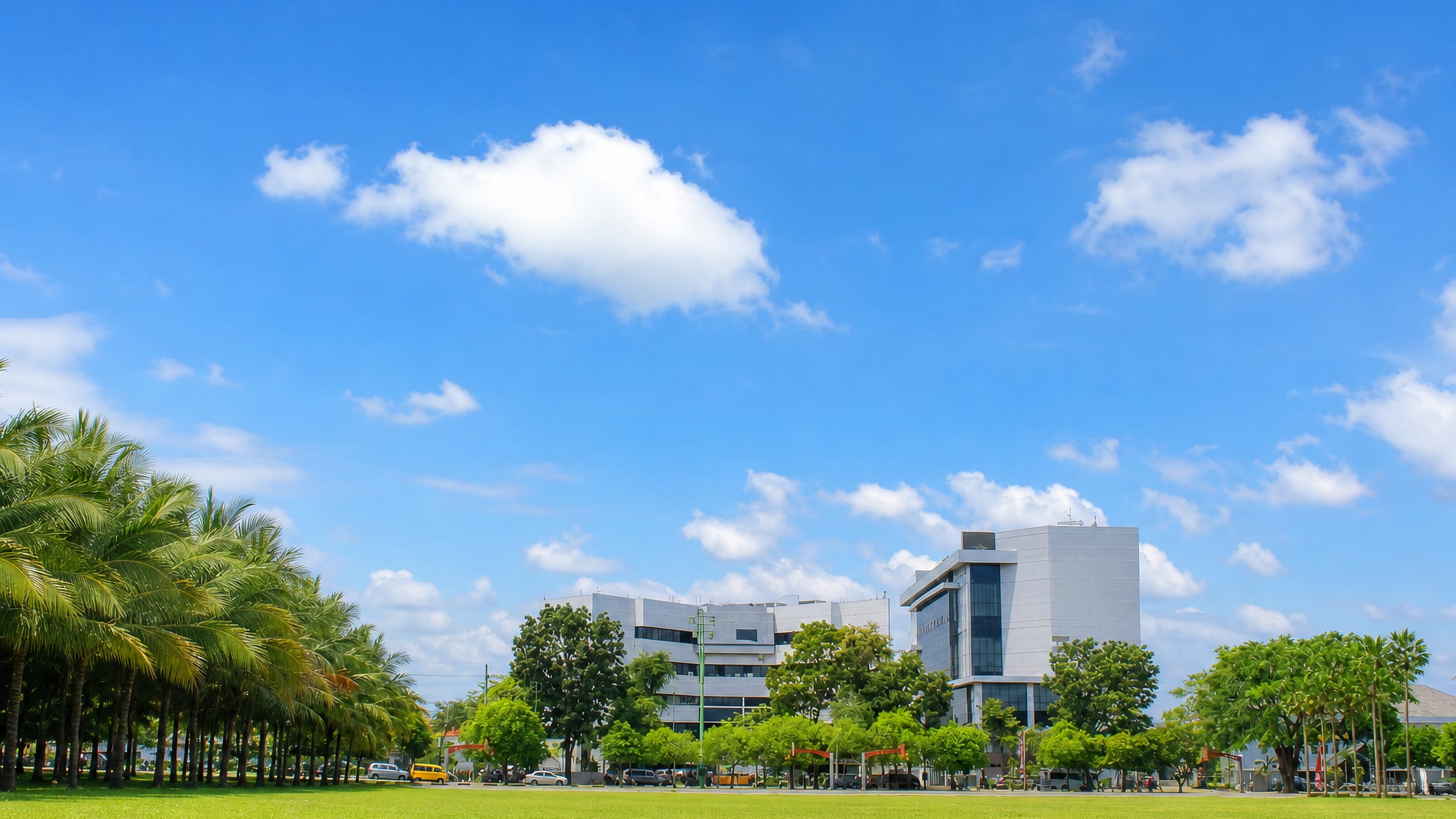 Palm-lined lawn in front of modern white campus buildings under a wide blue sky in Jember, East Java.