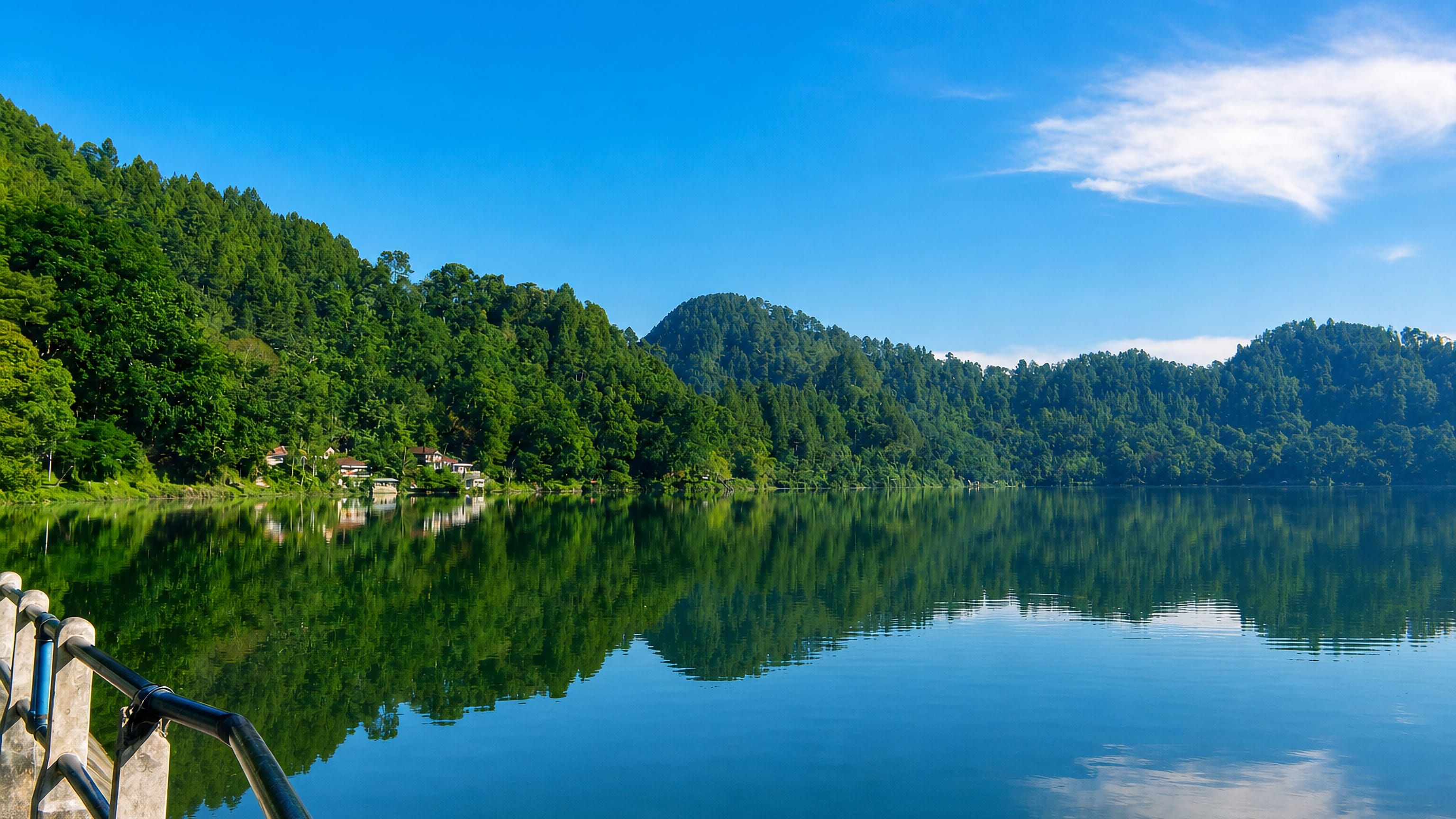 Forested crater lake ringed by hills near Ponorogo, East Java, mirrored in still water.