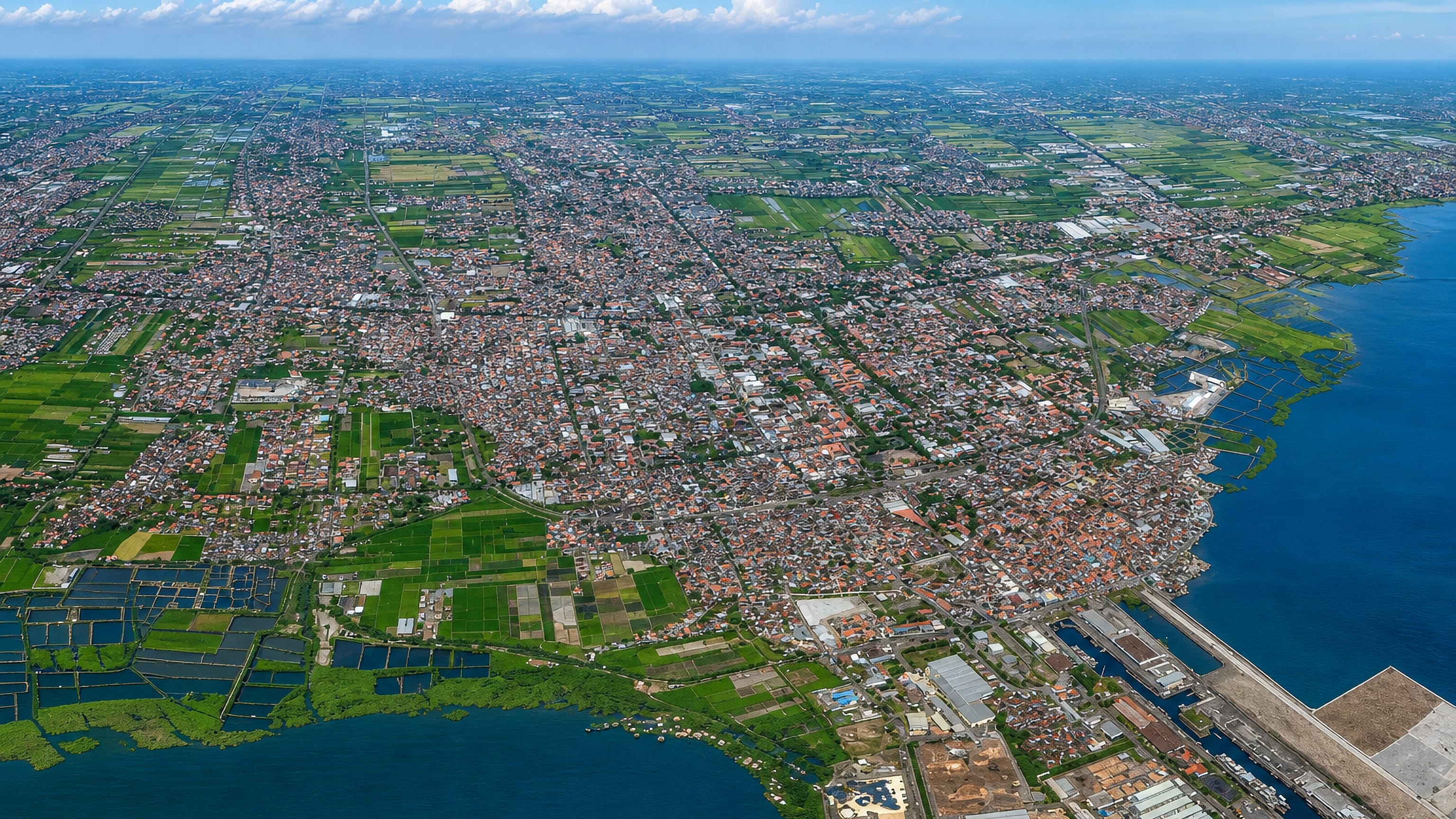 Aerial view of Probolinggo on Java's north coast, dense red-roofed blocks between rice fields, fish ponds and the sea.