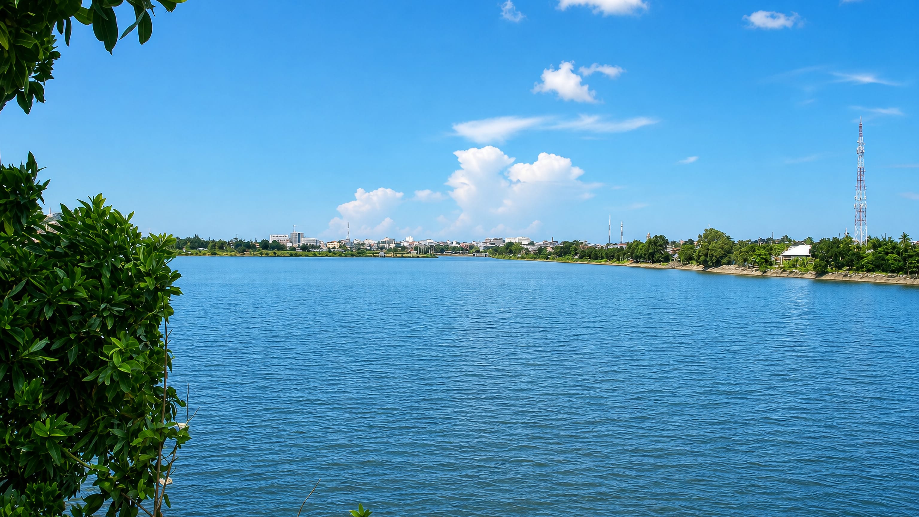Wide river reach with the low skyline and telecom mast of Pangkalpinang, Bangka Island, Indonesia.
