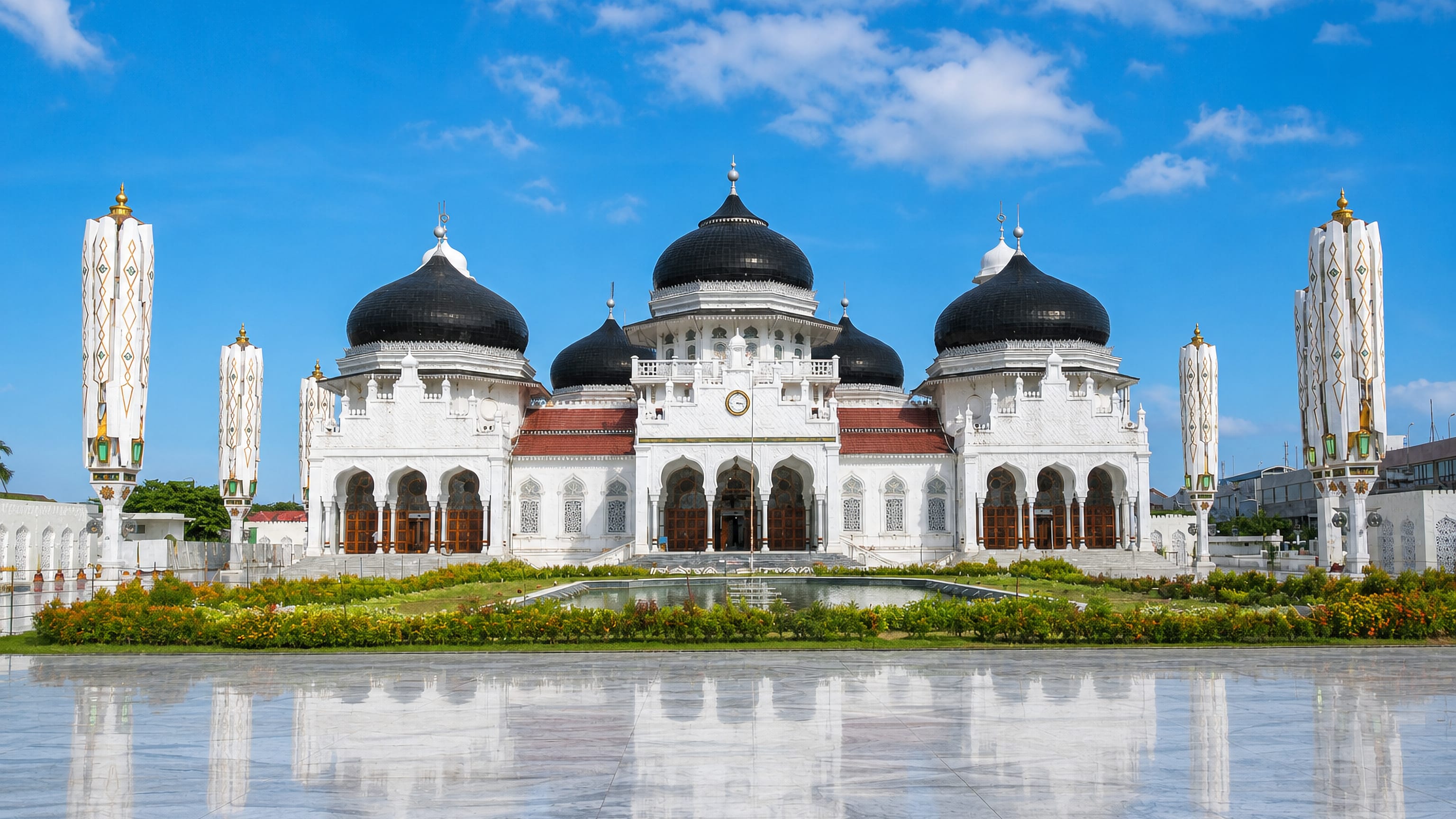 The white Baiturrahman Grand Mosque with its black domes and reflecting pool in Banda Aceh, Indonesia