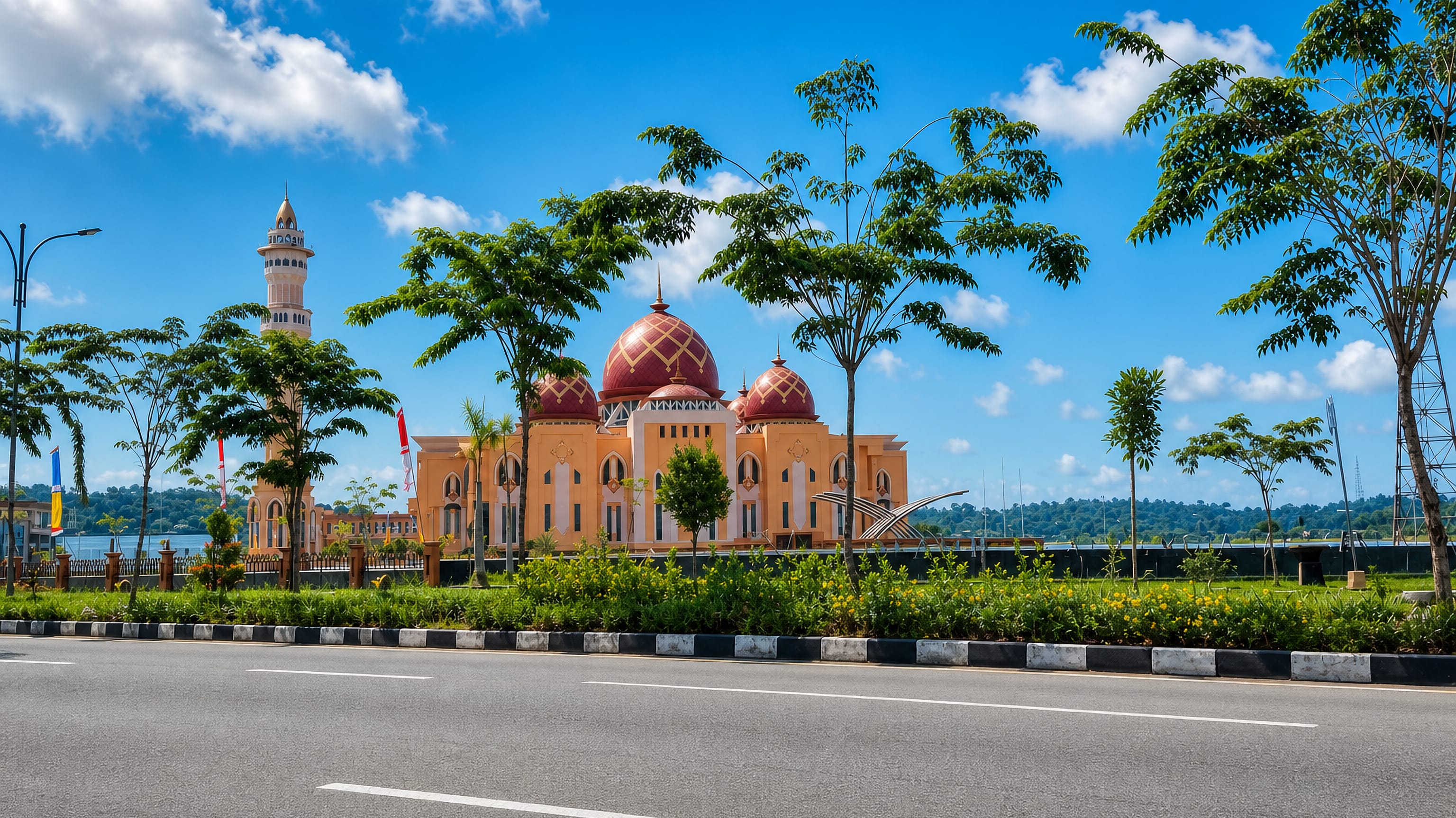 Waterfront grand mosque with red domes and a tall minaret seen past a palm-lined road in Tarakan, Indonesia.