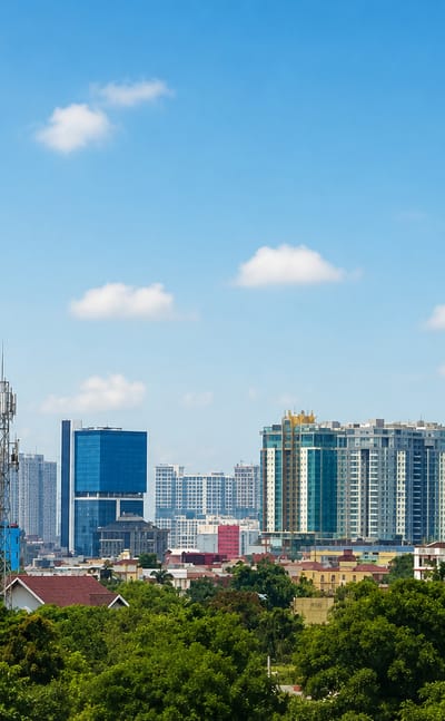 Medan skyline of high-rise towers rising behind a belt of green tropical trees under a bright blue sky