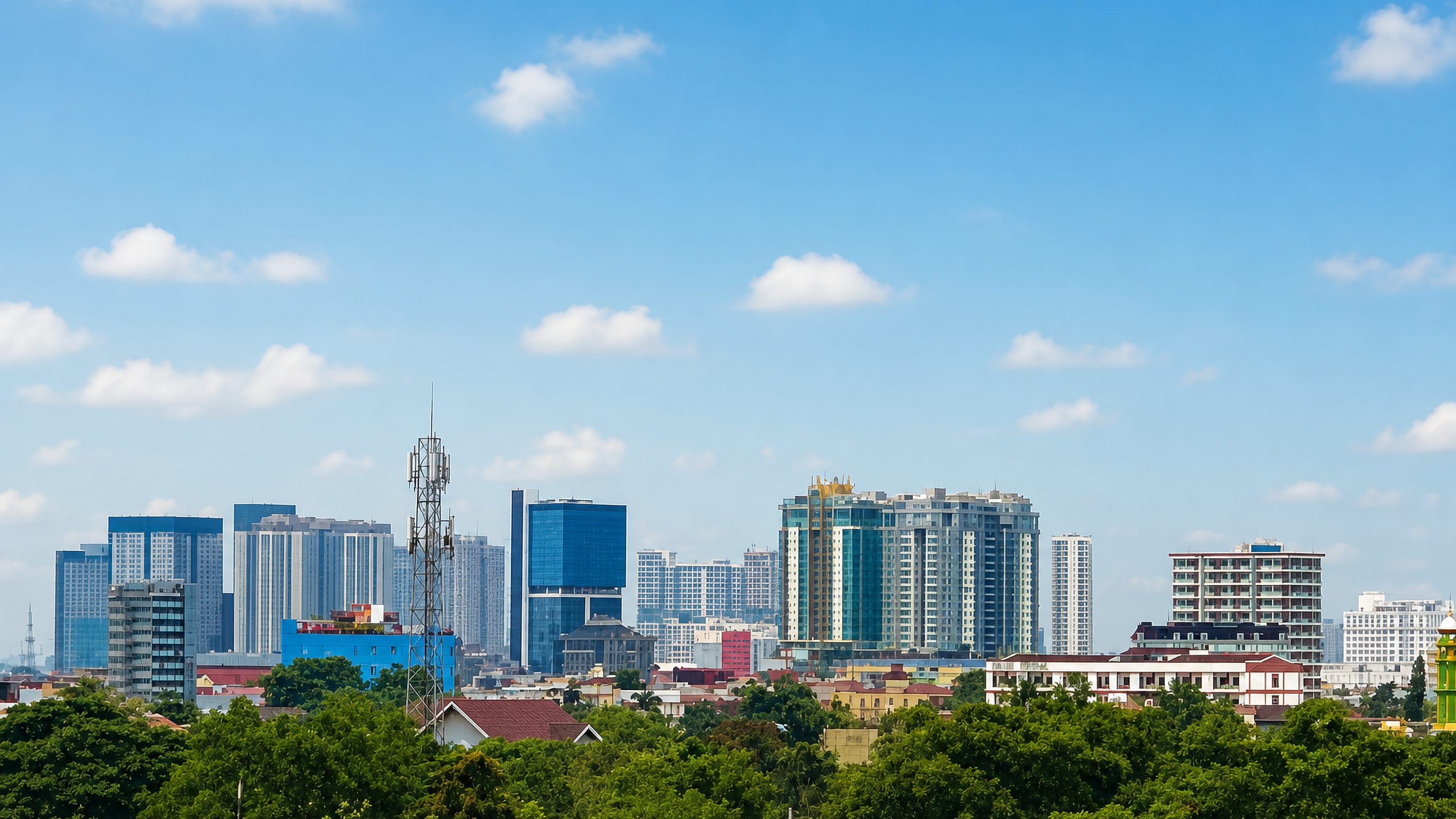 Medan skyline of high-rise towers rising behind a belt of green tropical trees under a bright blue sky