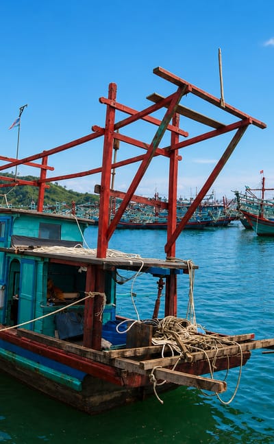 Wooden fishing boats moored at the harbour in Sibolga, Indonesia, with green hills across the bay.