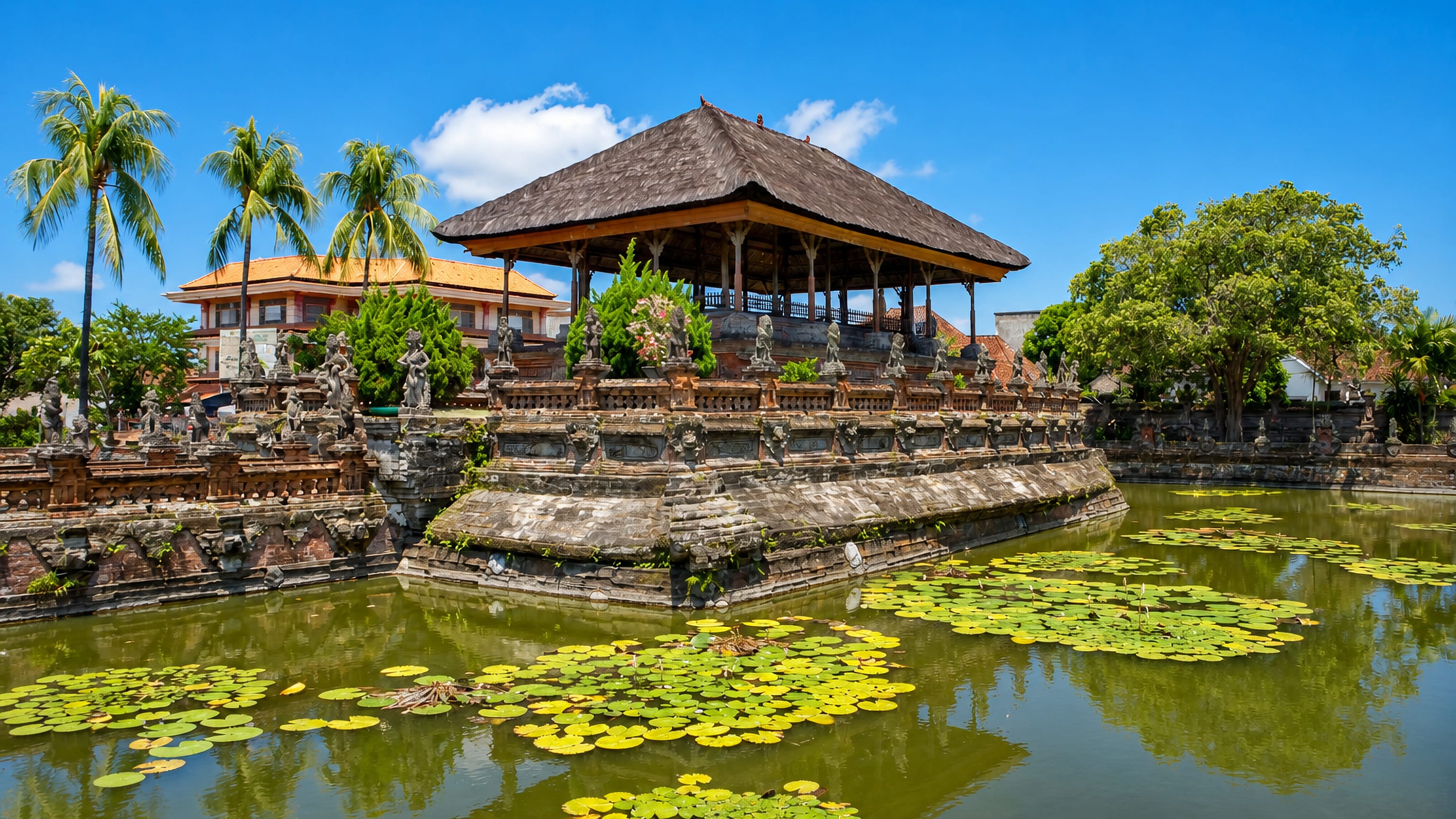 Kertha Gosa floating pavilion and lily pond in Klungkung, Bali, framed by palms under a bright blue sky.