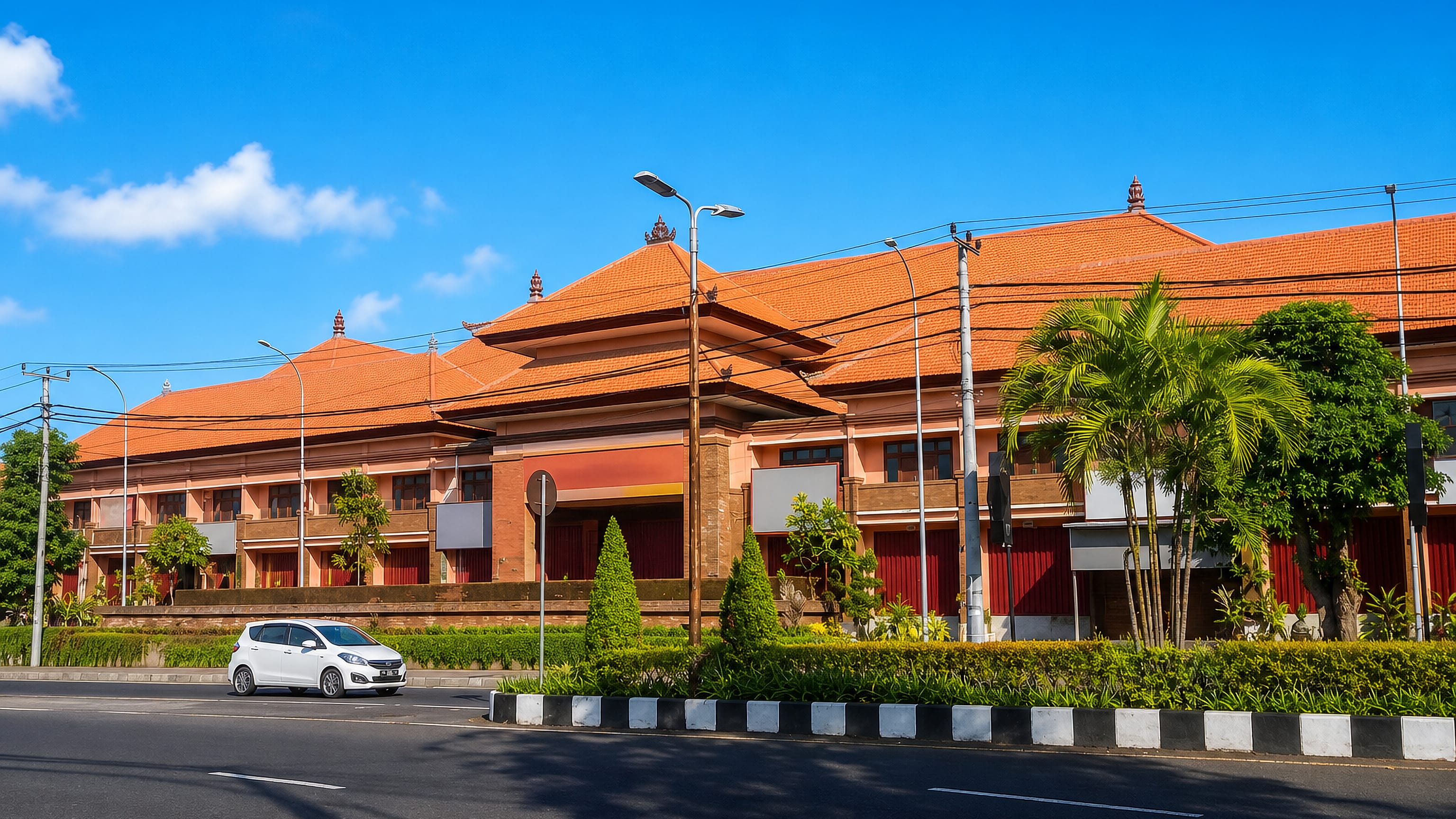 Balinese red-tile pavilions line a wide street in Singaraja, north Bali, under a bright blue sky.