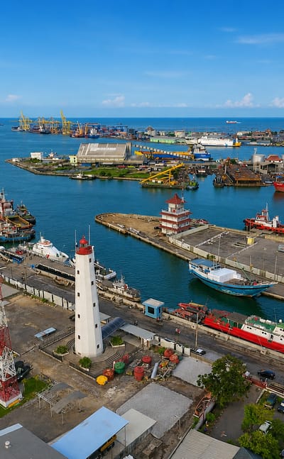 Semarang's Tanjung Emas port with a white lighthouse, moored ships, cranes and grain silos along the waterfront.