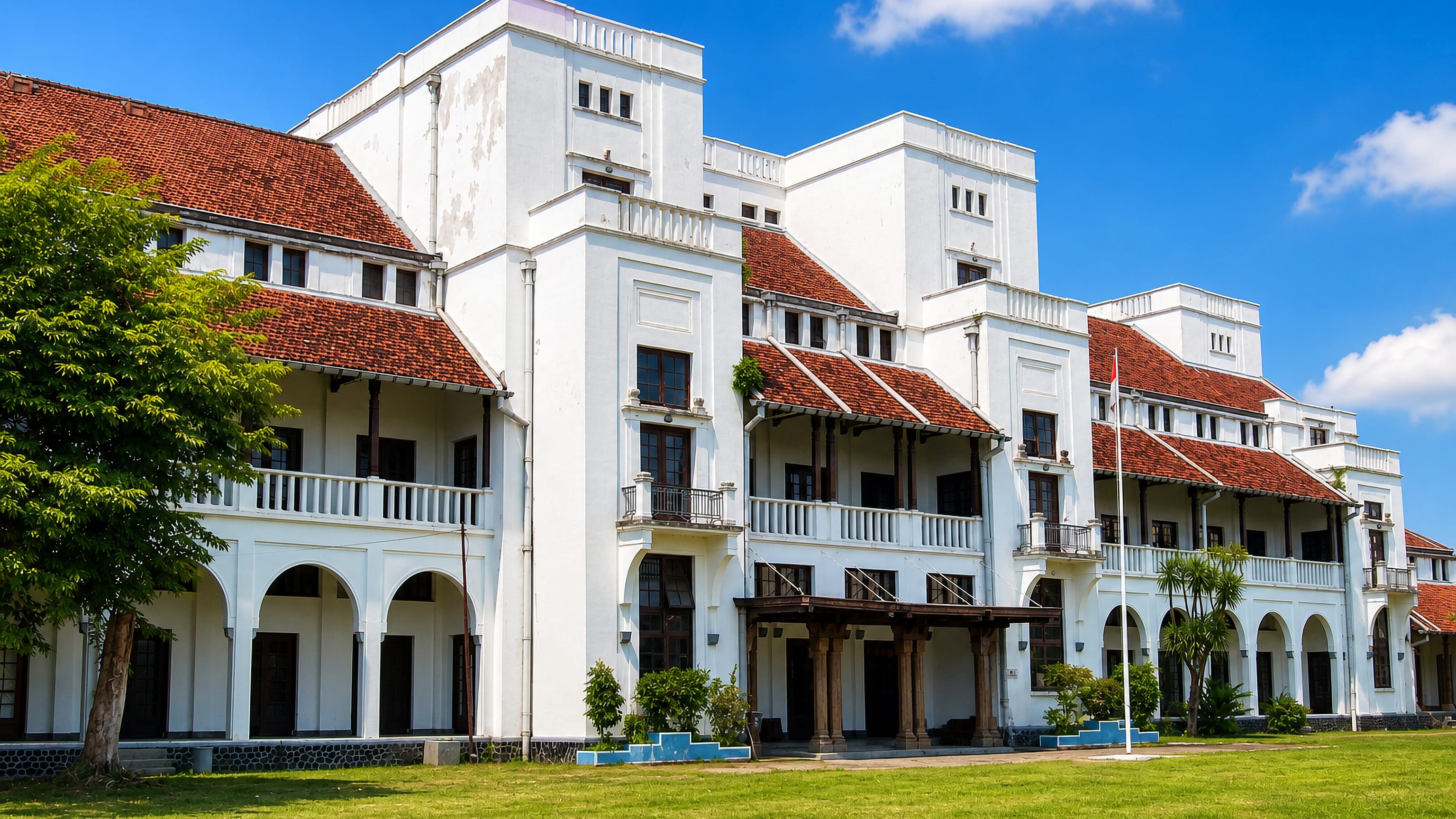 White Dutch colonial building with red tile roofs and arcades on a lawn in Tegal, Indonesia.