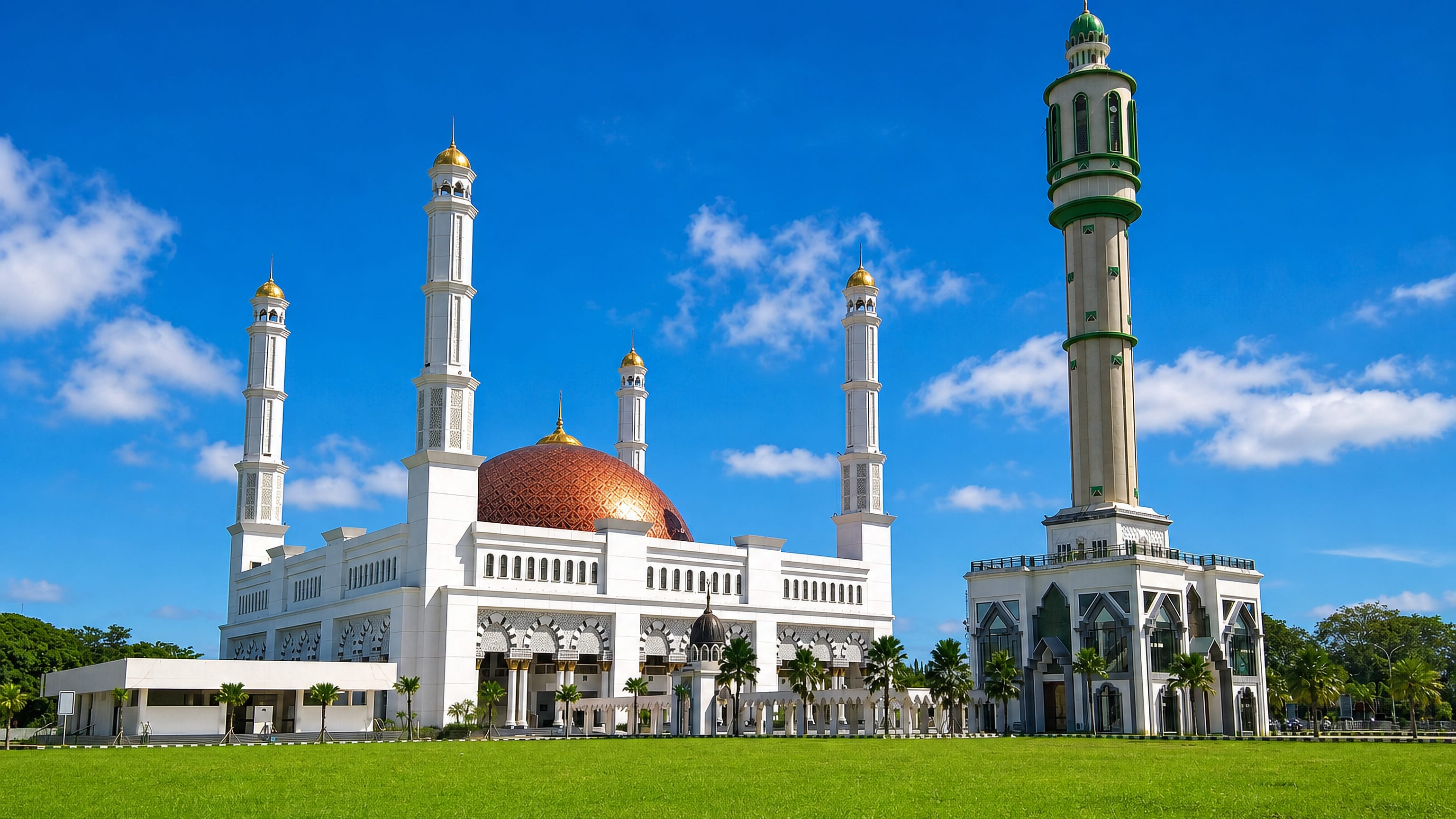 White mosque with a copper dome and a tall standalone minaret above a green lawn in Pontianak, West Kalimantan