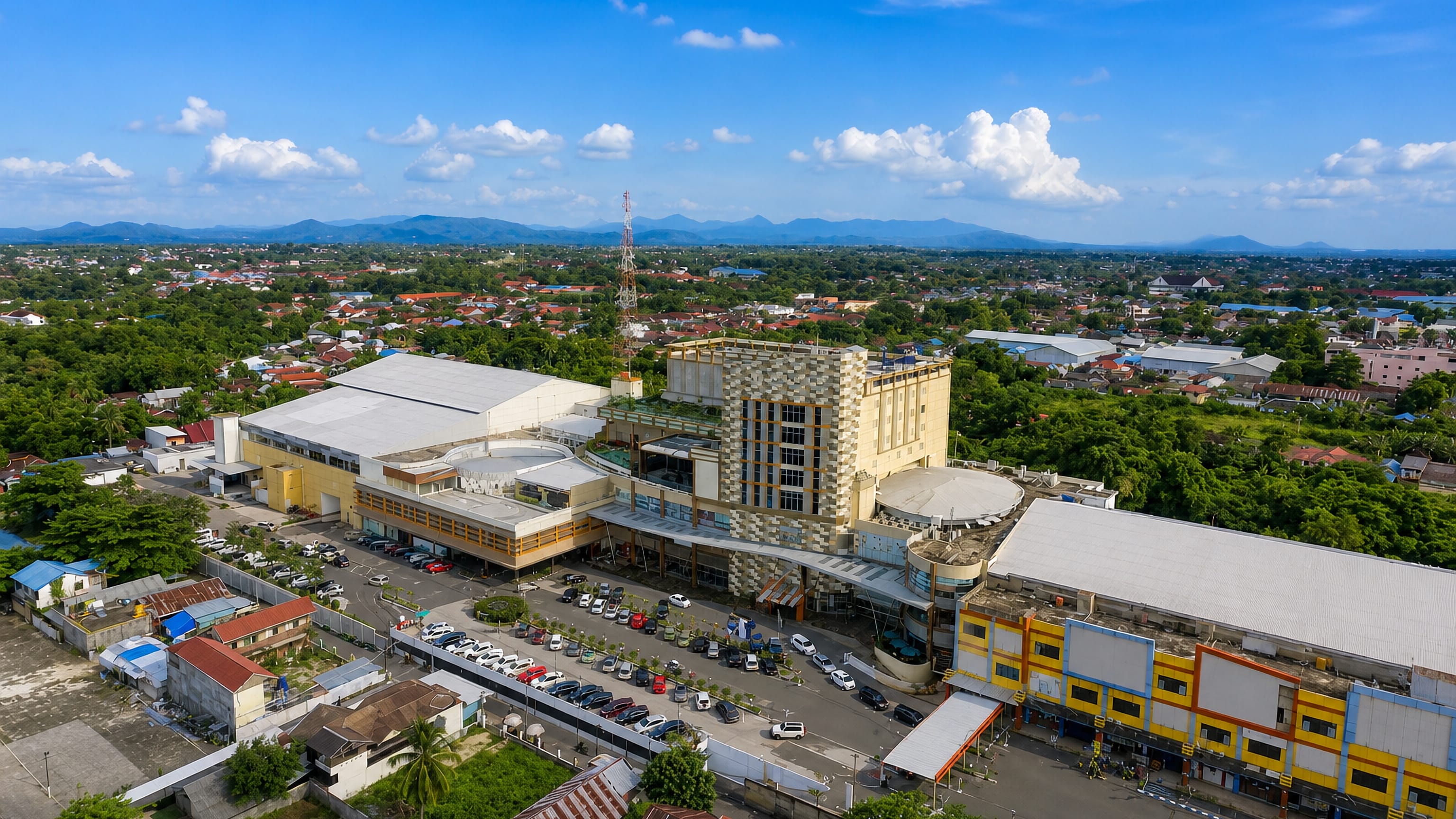 Aerial view of central Banjarbaru, Indonesia, with a shopping complex, tiled roofs and distant hills.