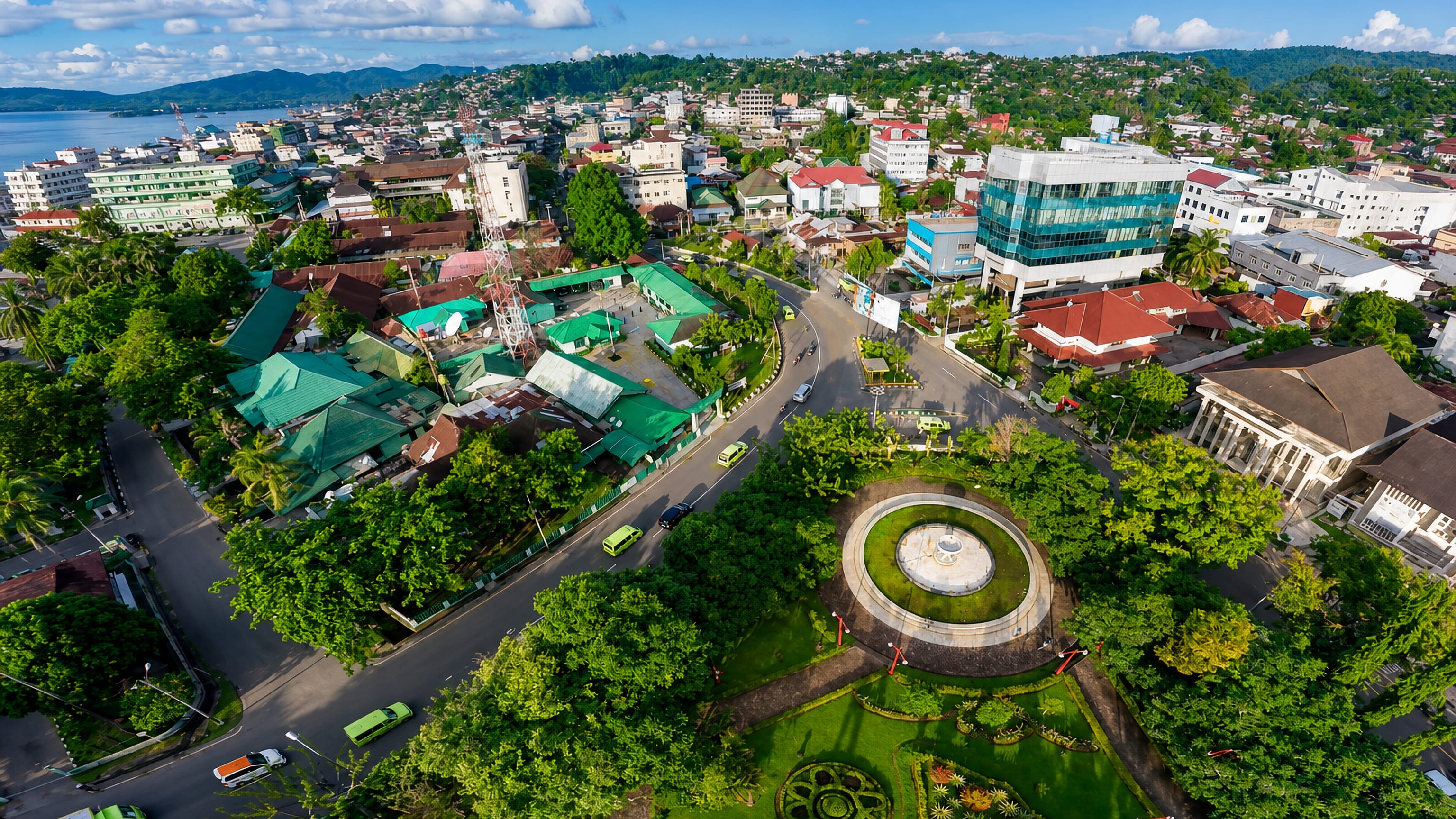 Aerial view over central Ambon, Indonesia, with a landscaped roundabout, red-roofed houses and the bay beyond.