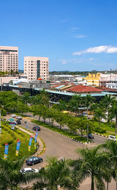 Batam townscape with a hotel tower, palm-lined boulevard and roundabout under a tropical blue sky