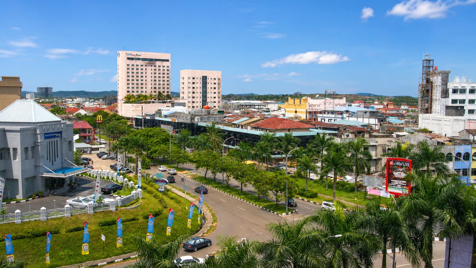 Batam townscape with a hotel tower, palm-lined boulevard and roundabout under a tropical blue sky