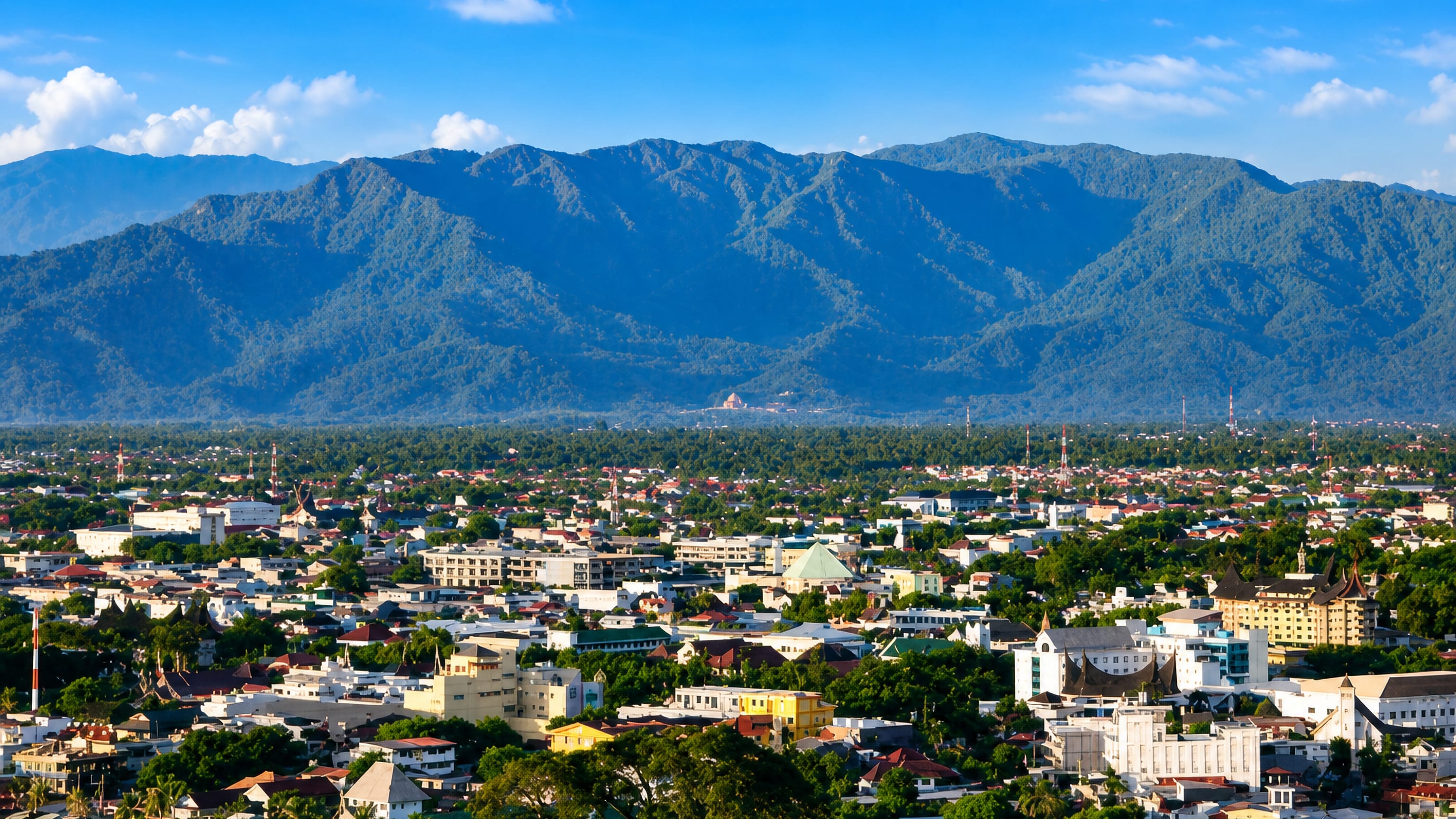 Padang, West Sumatra, spreading toward the Bukit Barisan range, with Minangkabau horned roofs among low-rise blocks.
