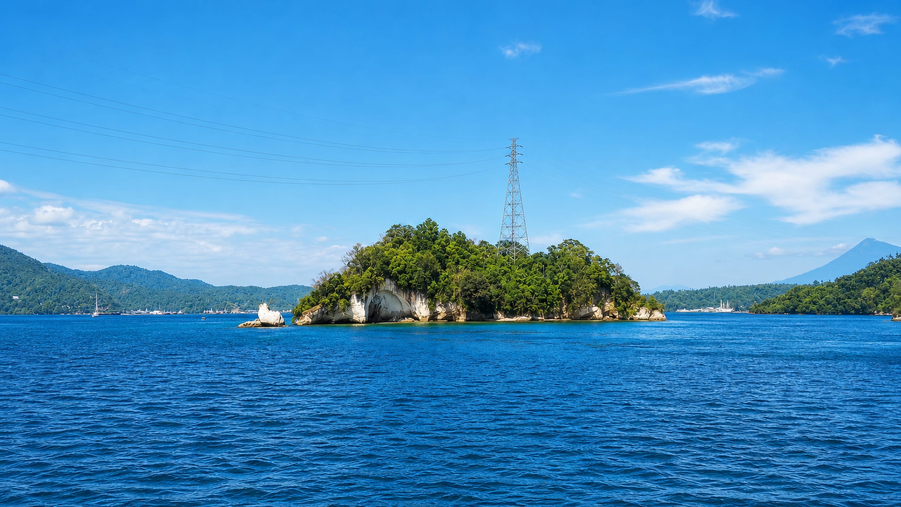 Forested islet and a distant volcano across the strait at Bitung, North Sulawesi, Indonesia