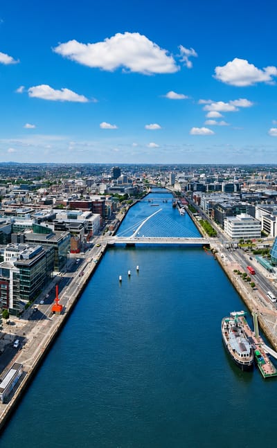 Aerial view of Dublin's River Liffey and docklands lined with modern quays and bridges under blue sky.