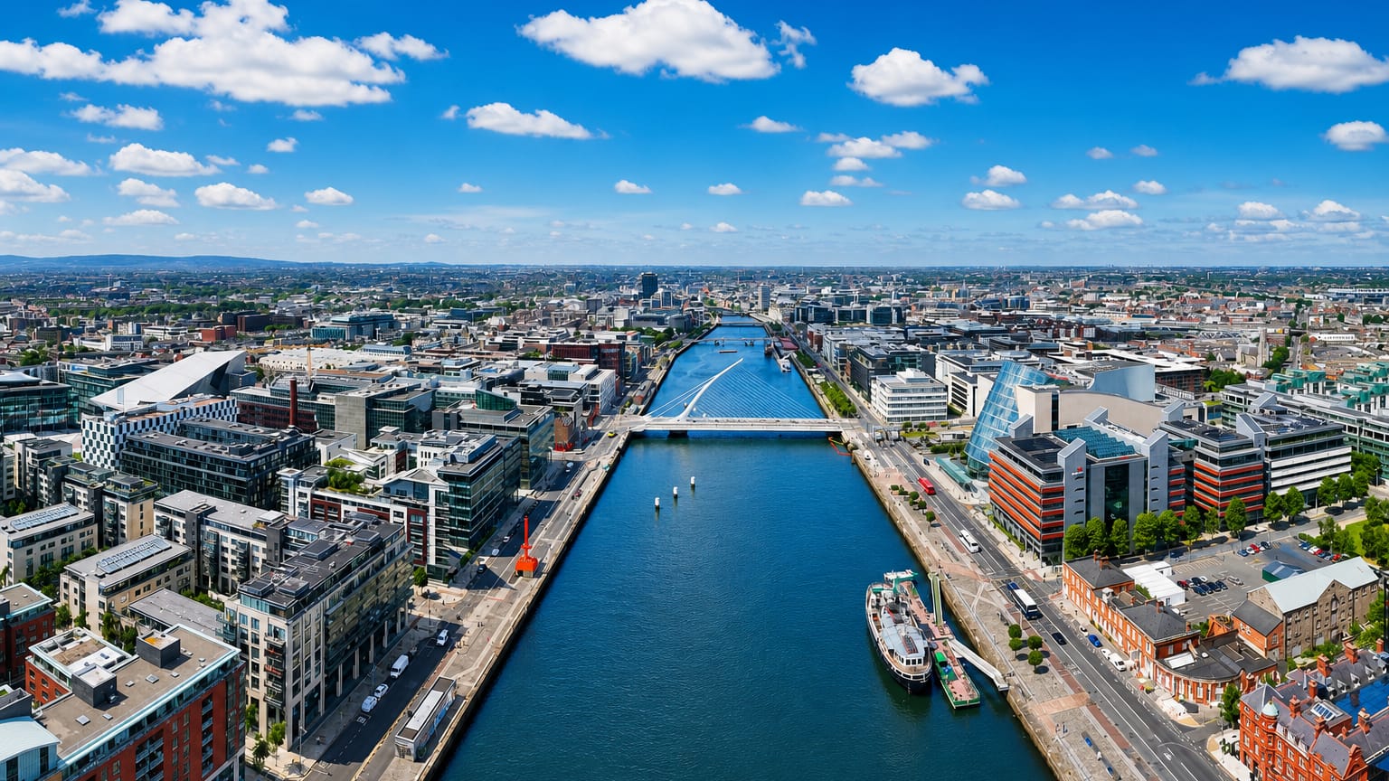Aerial view of Dublin's River Liffey and docklands lined with modern quays and bridges under blue sky.