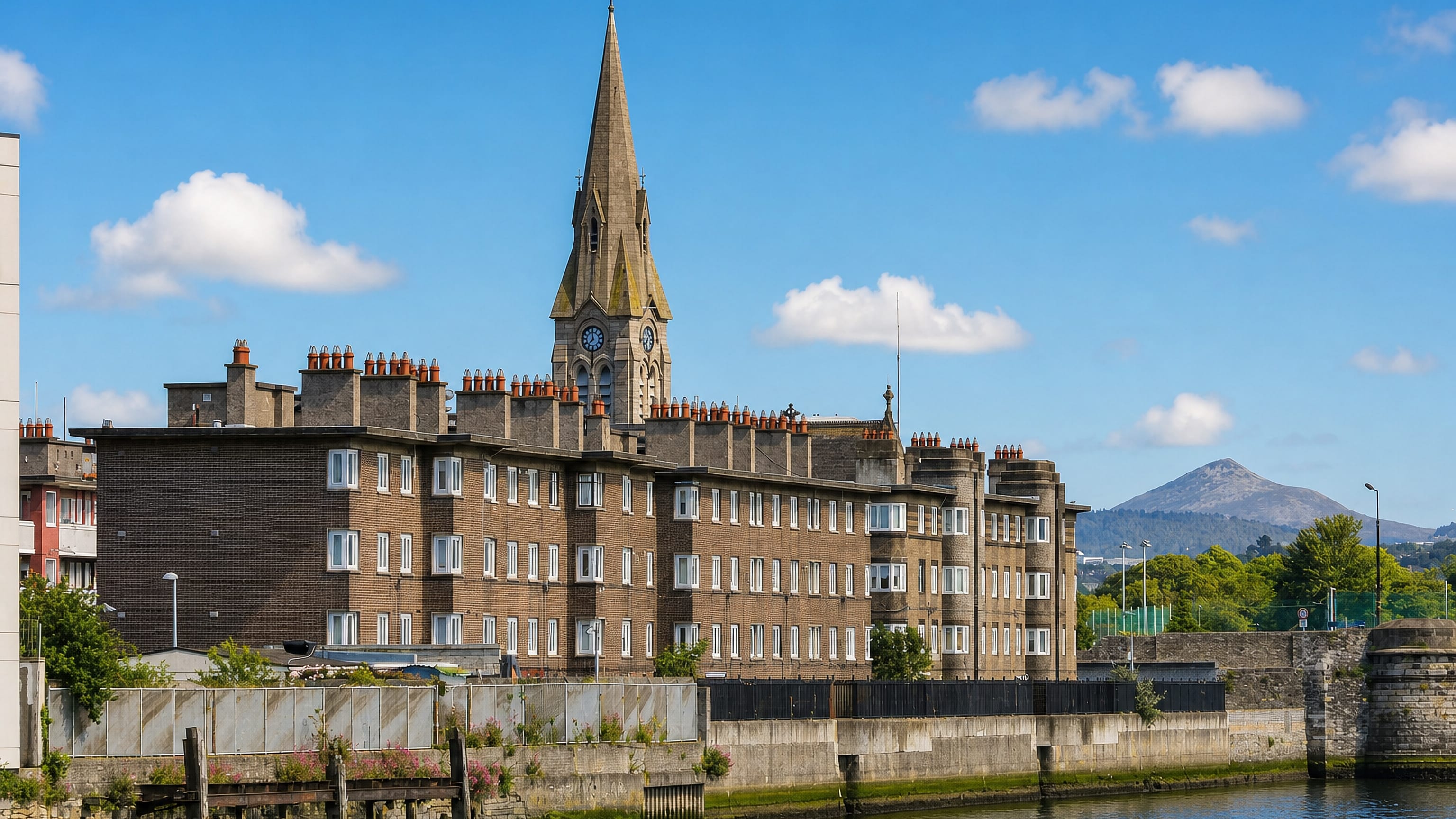 Red-brick apartment terrace and church spire above the quayside water in Ringsend, Dublin.