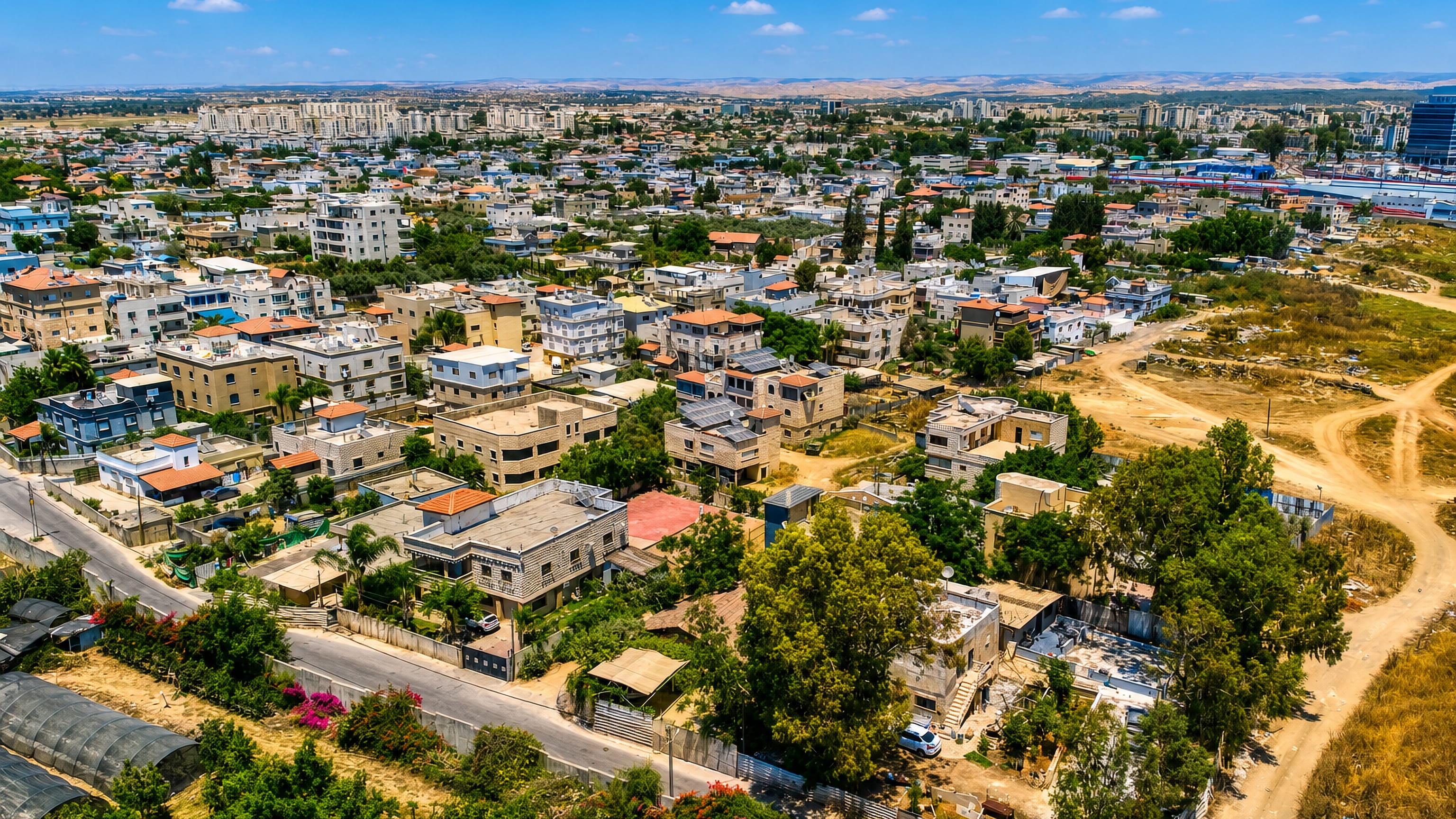 Aerial view of Lod, Israel, with red-roofed low-rise houses, greenery and distant apartment towers.
