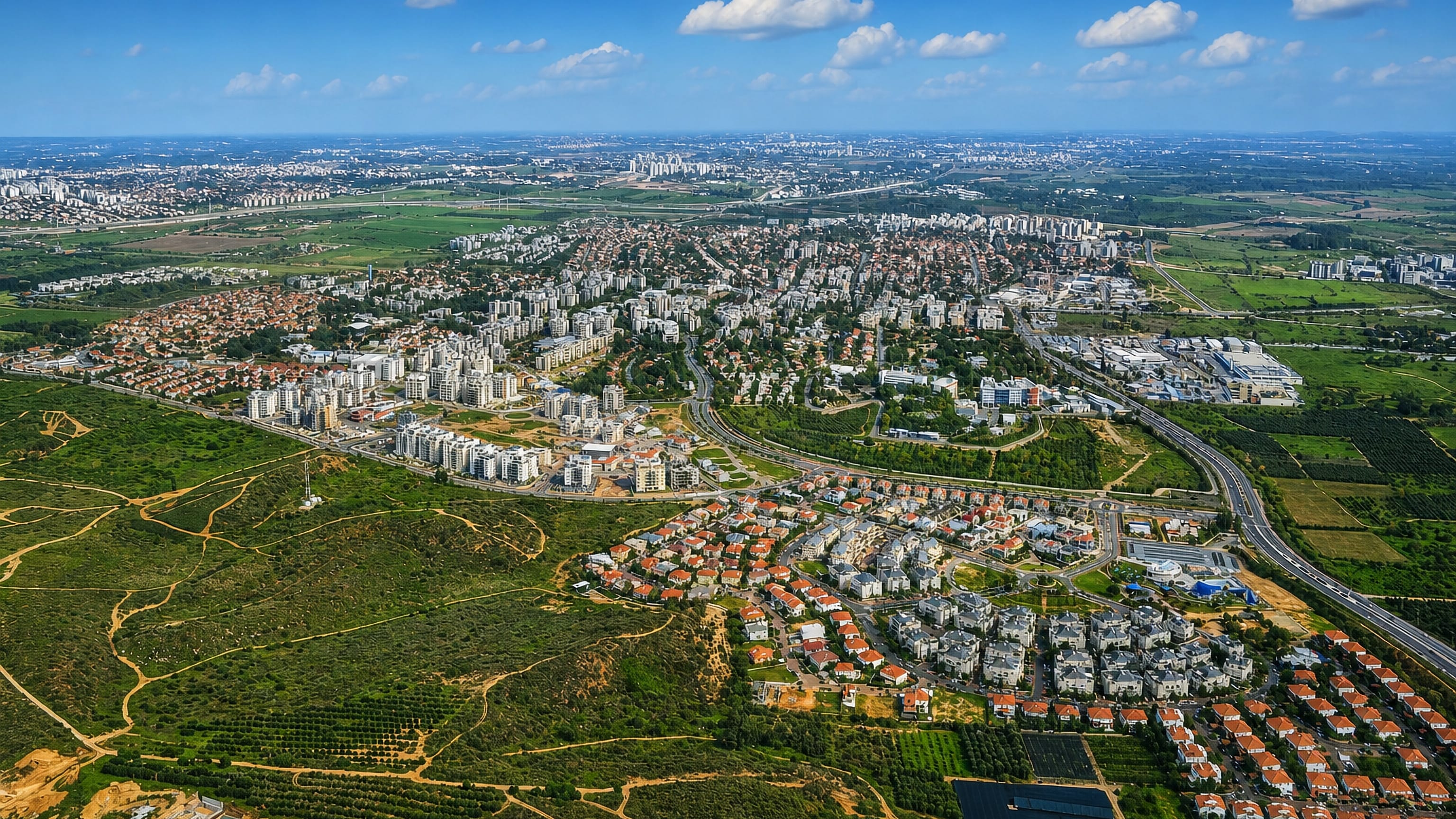 Aerial view of Ness Ziona, Israel, with apartment blocks, red-roofed houses and orchards toward the coast.