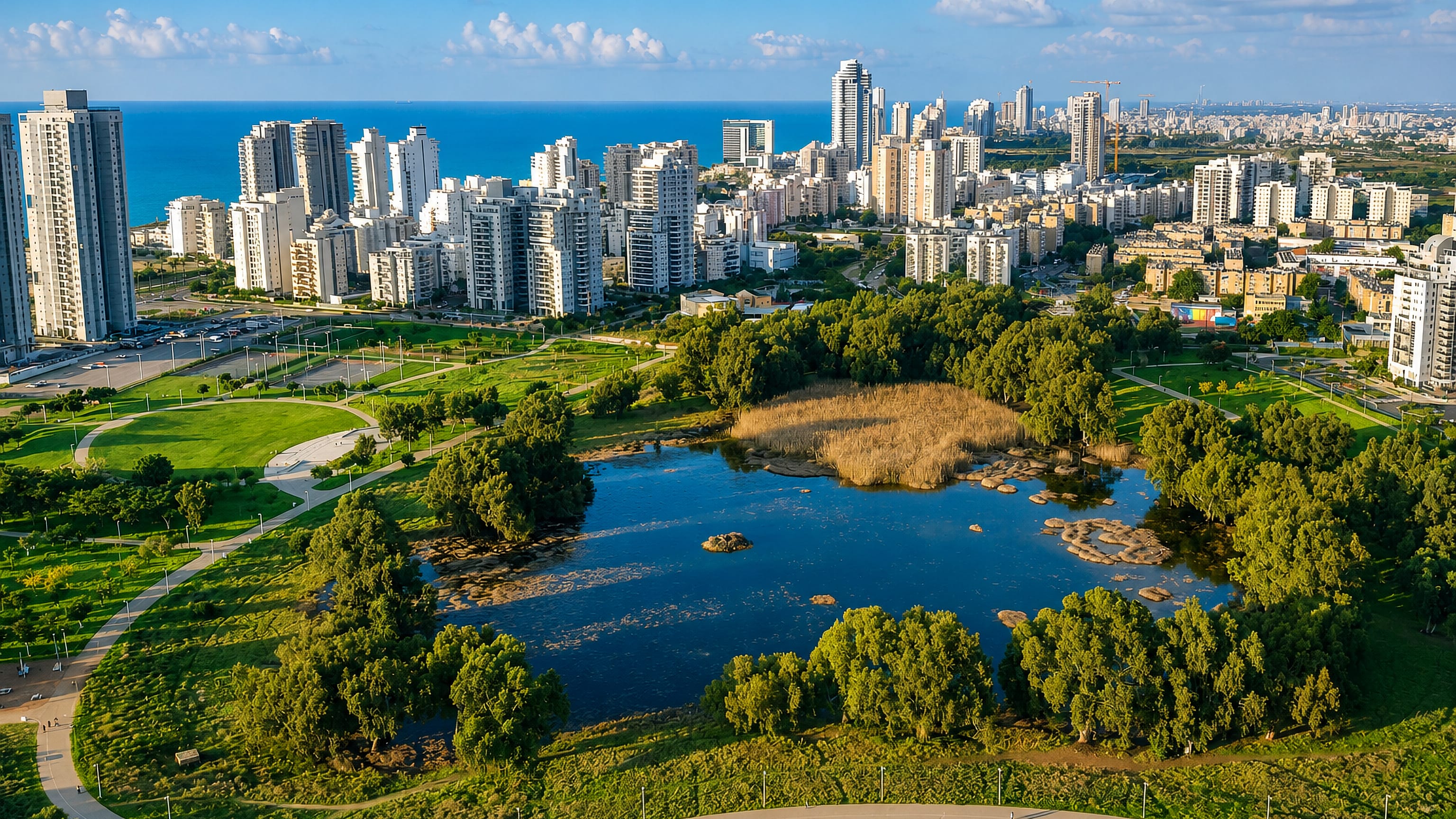 Aerial view of Netanya, Israel, with white residential towers above the Mediterranean and a green park lake.