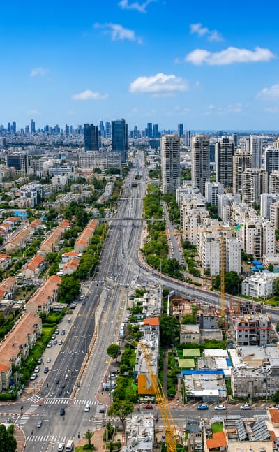 Aerial view of Petah Tikva, Israel, with a broad boulevard, white residential towers, and the distant Tel Aviv skyline.