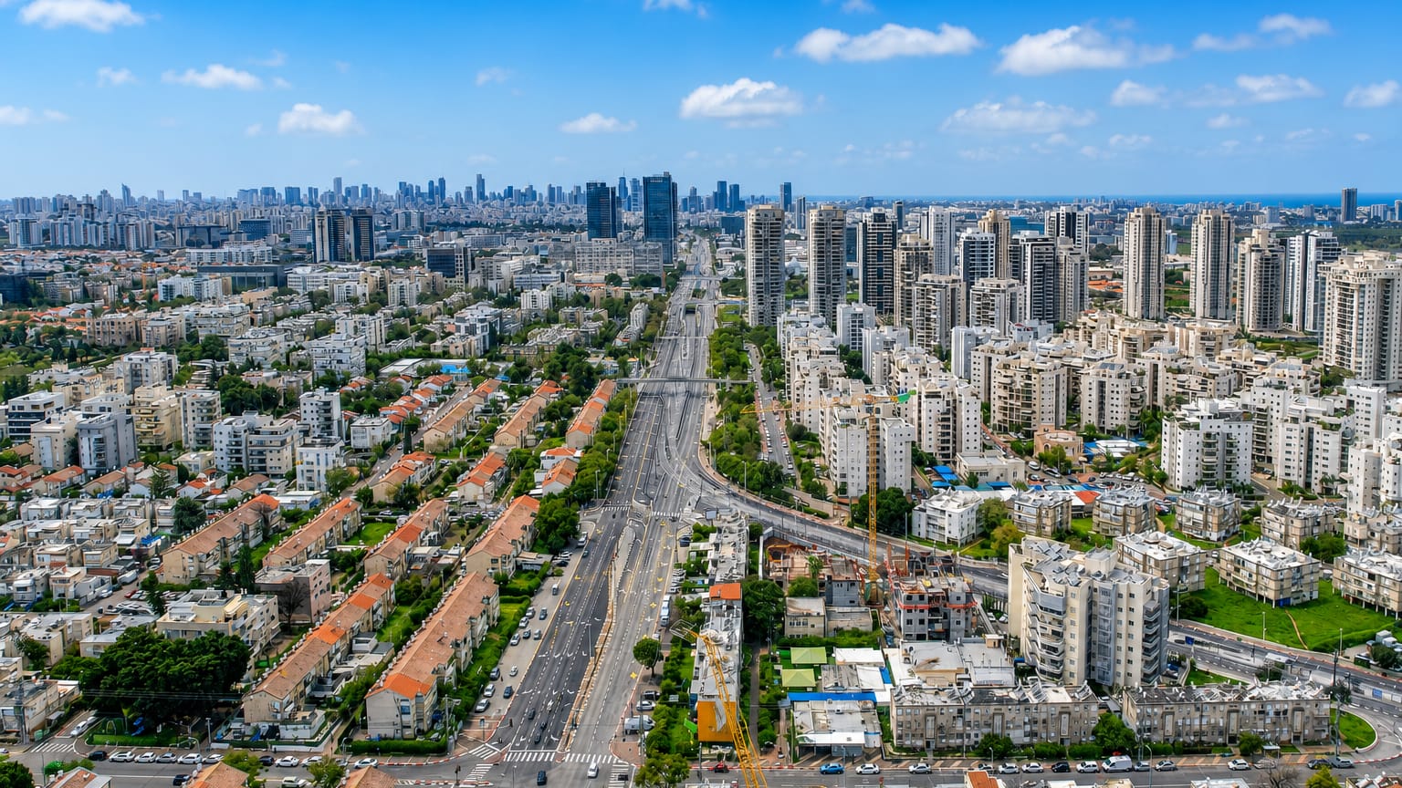 Aerial view of Petah Tikva, Israel, with a broad boulevard, white residential towers, and the distant Tel Aviv skyline.