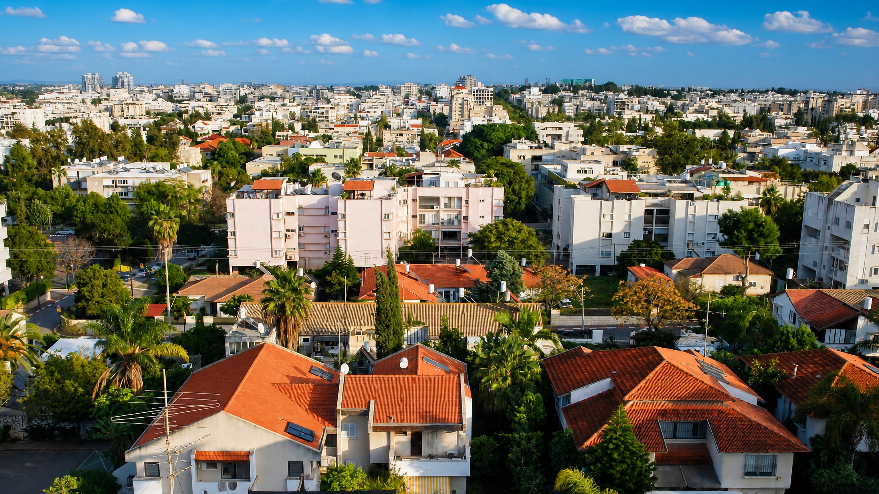 Red-tiled villas, apartment blocks and palm trees across Ra'anana, Israel, with towers on the horizon.
