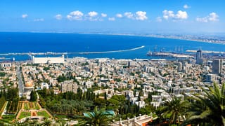 Haifa's Baha'i Gardens and golden-domed Shrine of the Bab descending toward the port and Mediterranean bay under a clear sky.