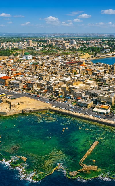 Aerial view of Acre's walled Old City on its peninsula with sea ramparts, harbor and the green-domed Al-Jazzar Mosque.