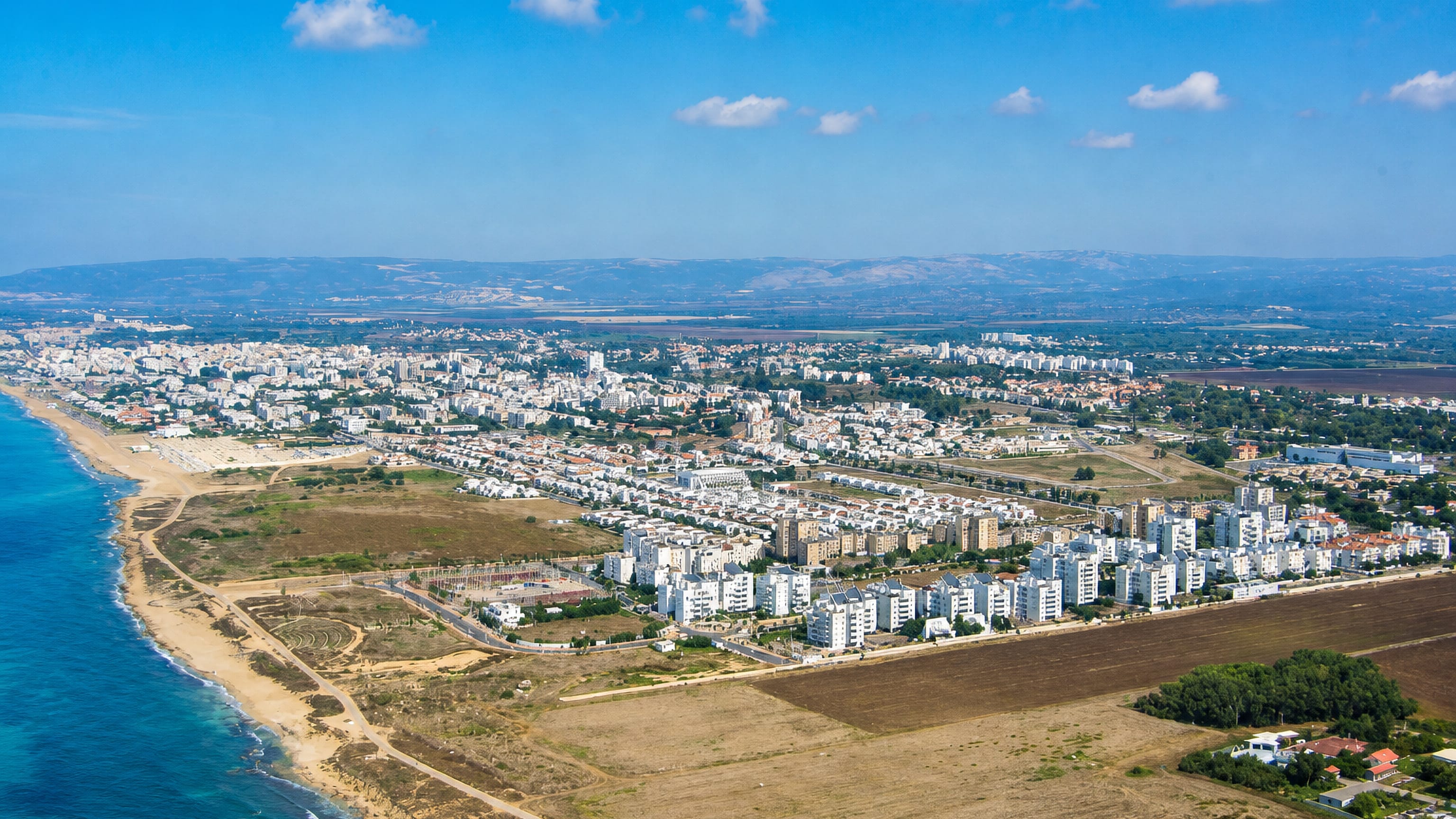 Aerial view of Nahariyya's Mediterranean shoreline, white apartment blocks and the Galilee hills beyond.