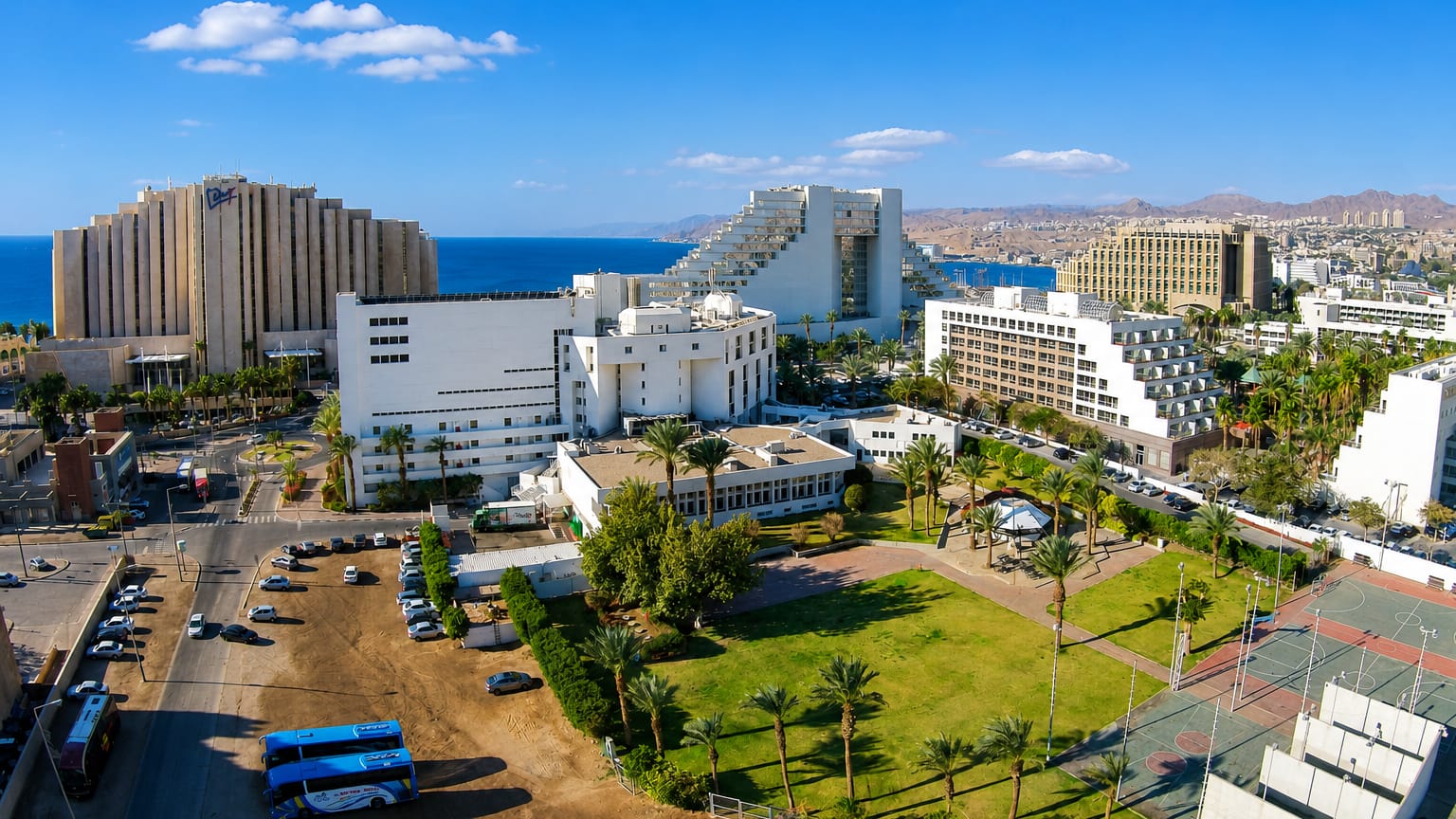 Aerial view of Eilat's Red Sea resort hotels and palm-lined grounds with desert mountains beyond.
