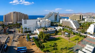 Aerial view of Eilat's Red Sea resort hotels and palm-lined grounds with desert mountains beyond.