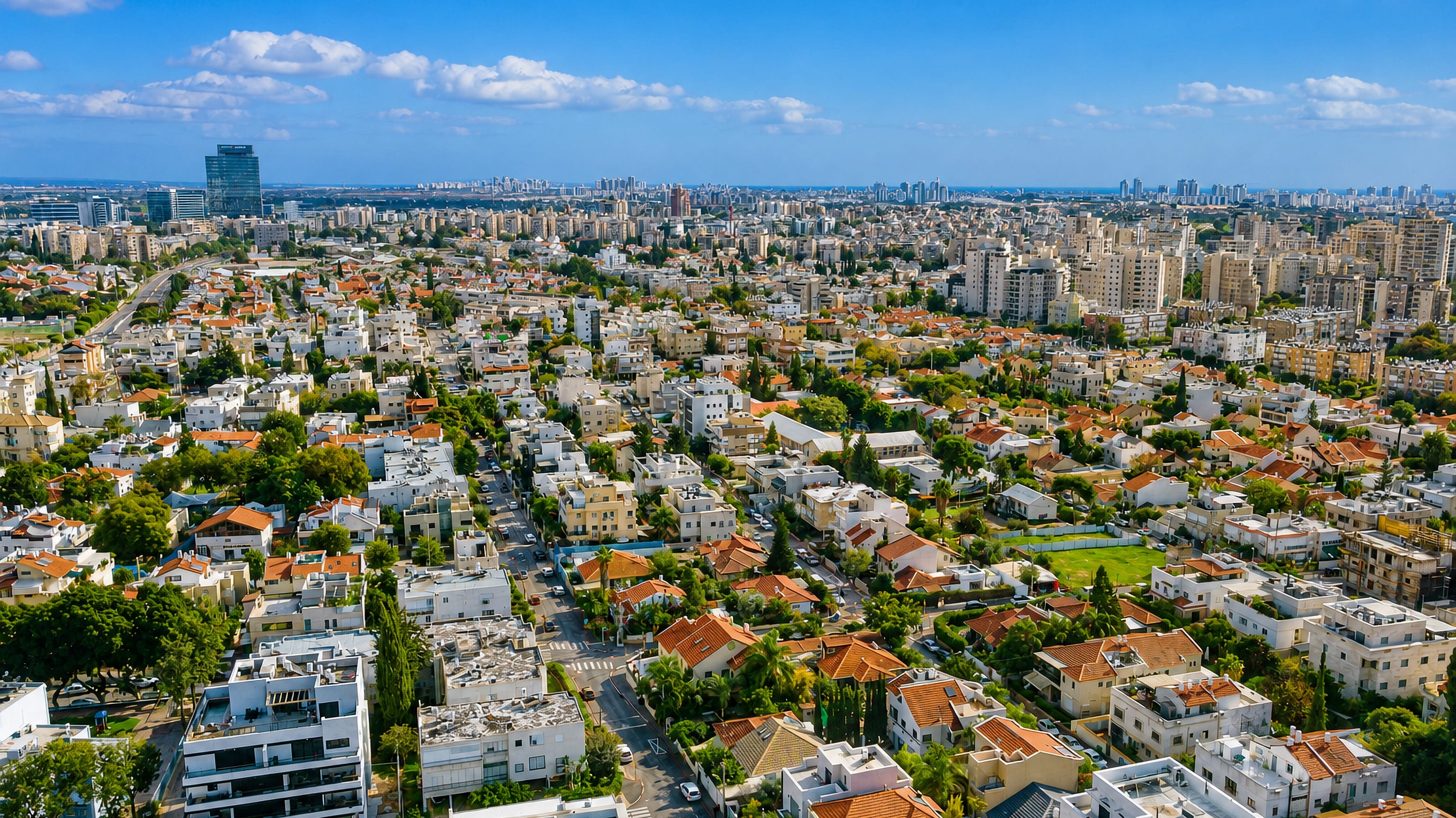 Aerial view over Holon's red-tiled houses and apartment blocks, with the Tel Aviv skyline on the horizon.