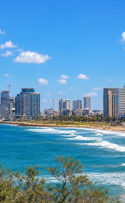 Tel Aviv beachfront skyline of high-rise towers above the Mediterranean shore with waves rolling onto the sand.