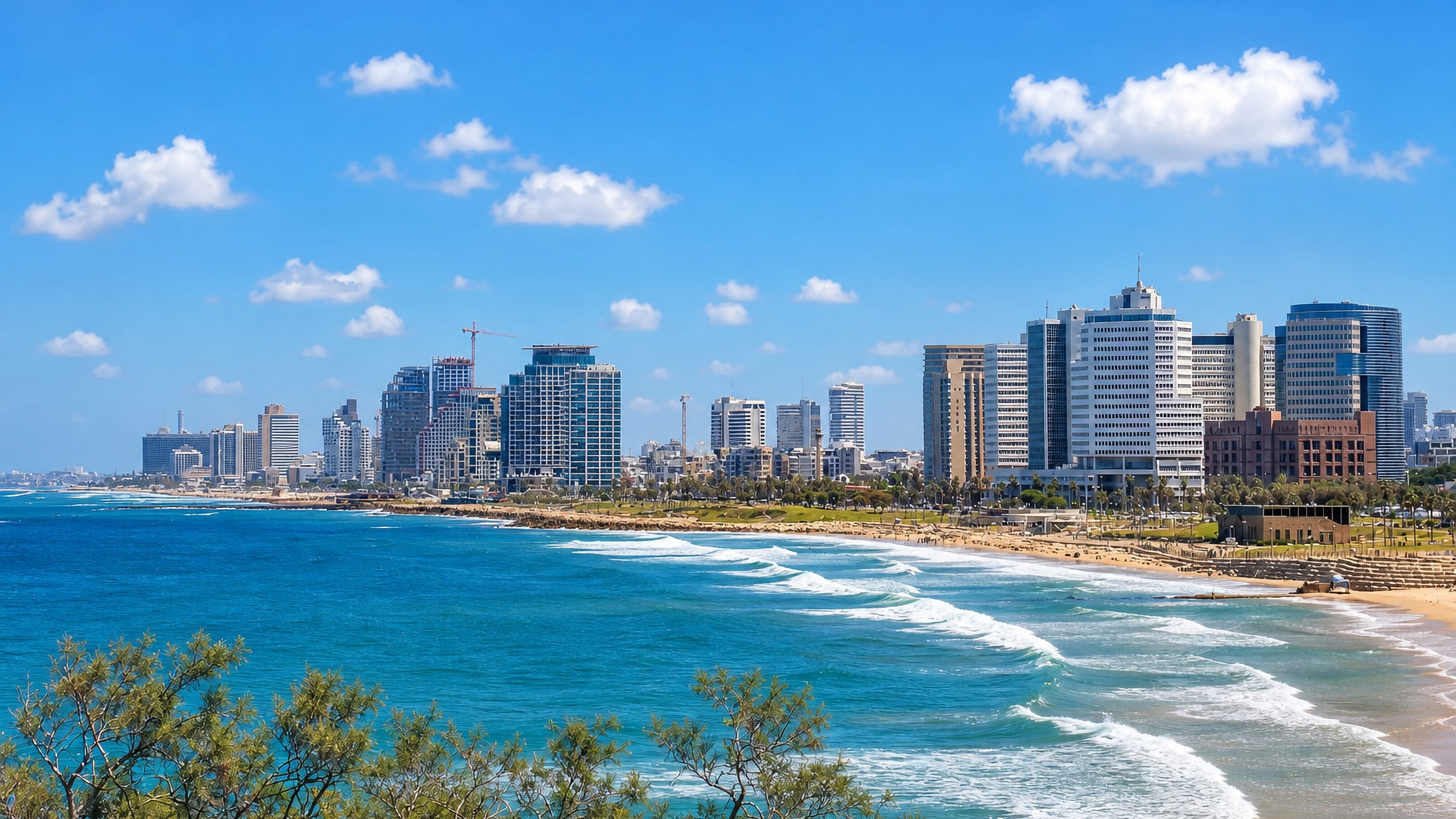 Tel Aviv beachfront skyline of high-rise towers above the Mediterranean shore with waves rolling onto the sand.