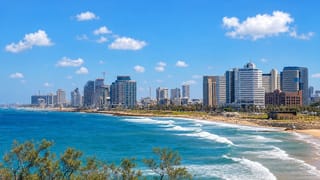 Tel Aviv beachfront skyline of high-rise towers above the Mediterranean shore with waves rolling onto the sand.