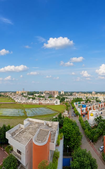 Rooftop panorama over Bhopal's suburban houses and green paddy fields under a wide blue sky, Madhya Pradesh.