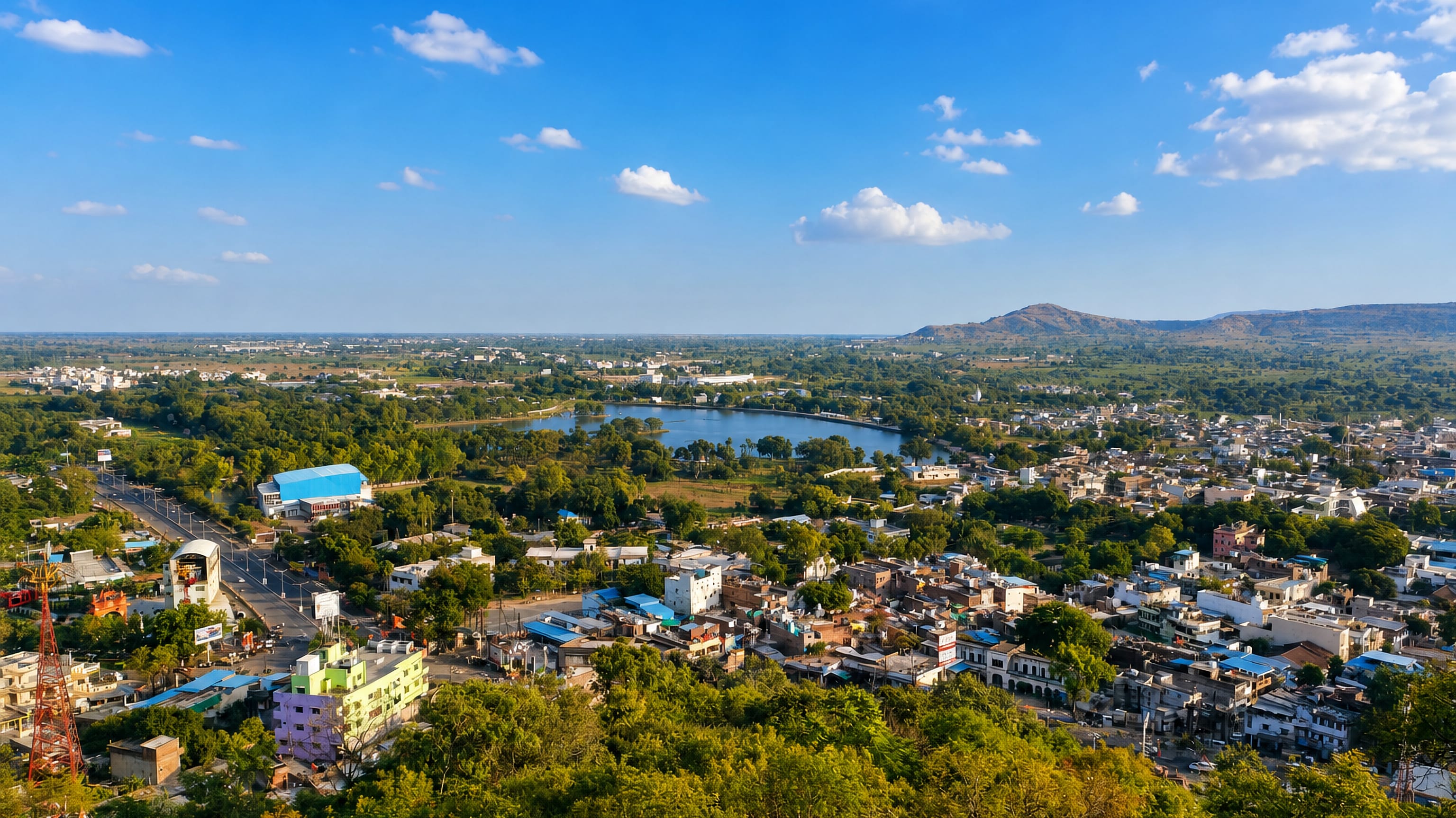 Hilltop view over Dewas, India, its low-rise streets and town lake framed by trees and distant hills.