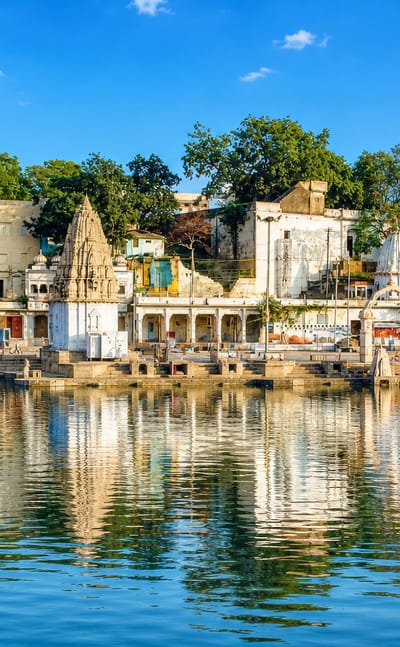 White temple spires along Ram Ghat on the Shipra River in Ujjain, India, reflected in the calm water.