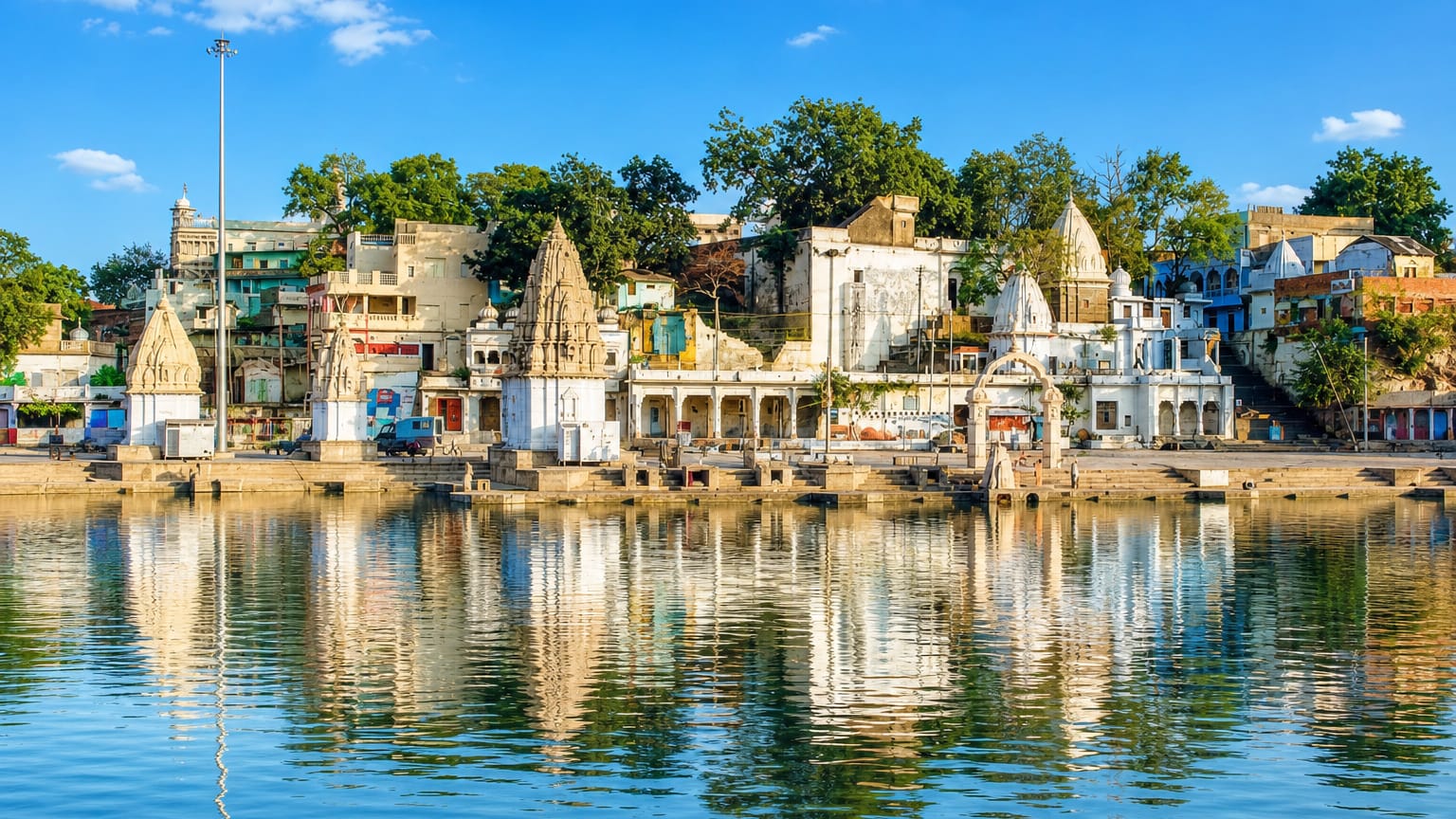 White temple spires along Ram Ghat on the Shipra River in Ujjain, India, reflected in the calm water.