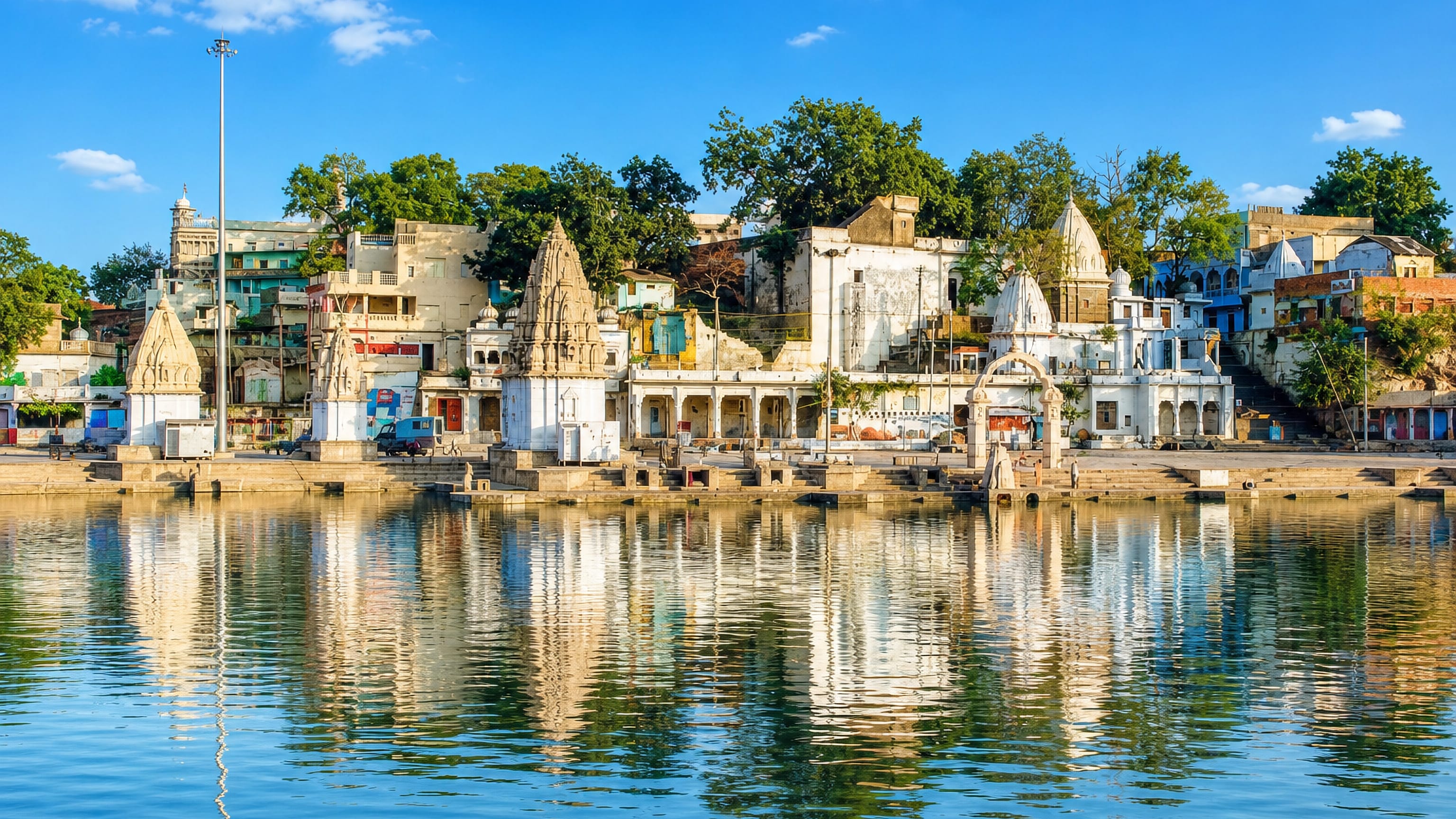 White temple spires along Ram Ghat on the Shipra River in Ujjain, India, reflected in the calm water.